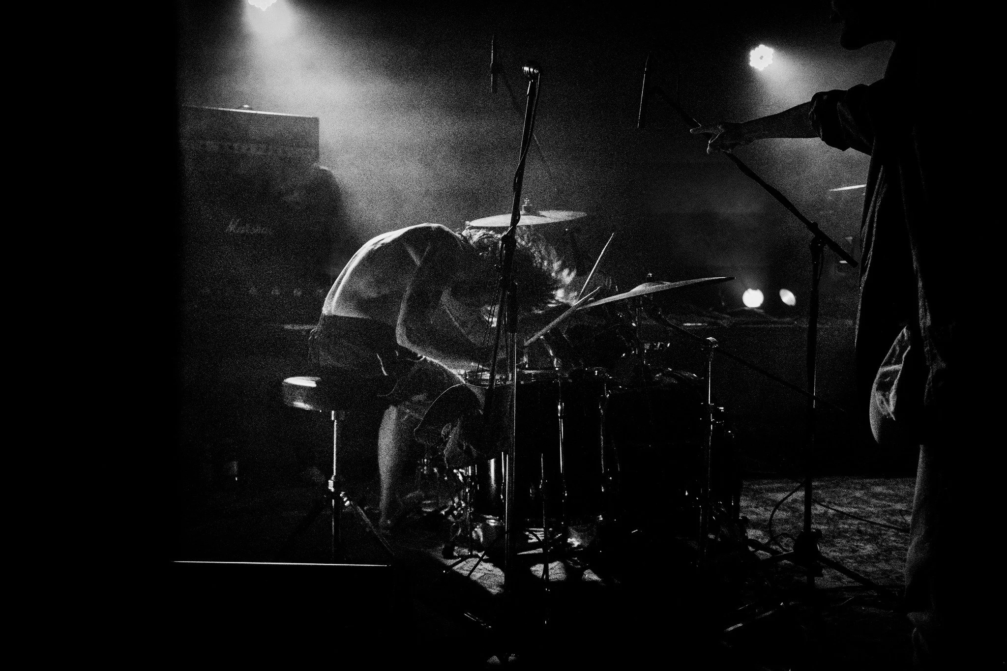Musicians performing on stage with drums, microphones, and stage lights in black and white.