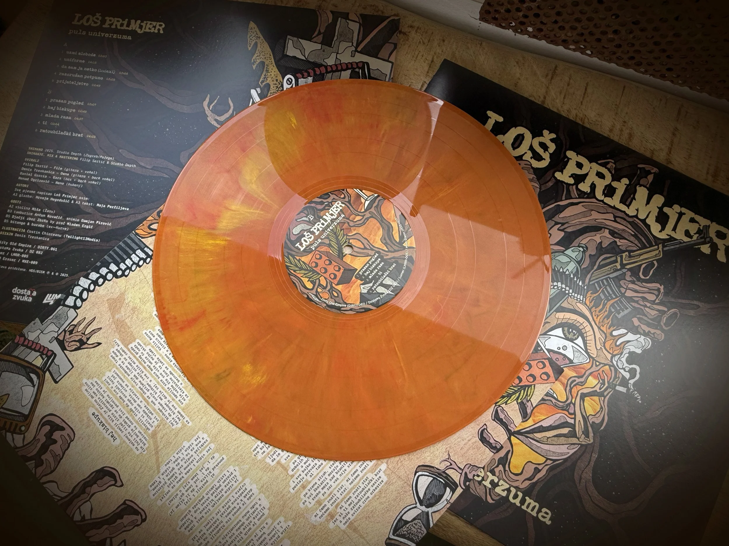 A decorative vinyl record with orange and yellow marbling placed on sheets of printed paper and artwork. The surroundings include graphic illustrations and text, possibly at a music or art event.