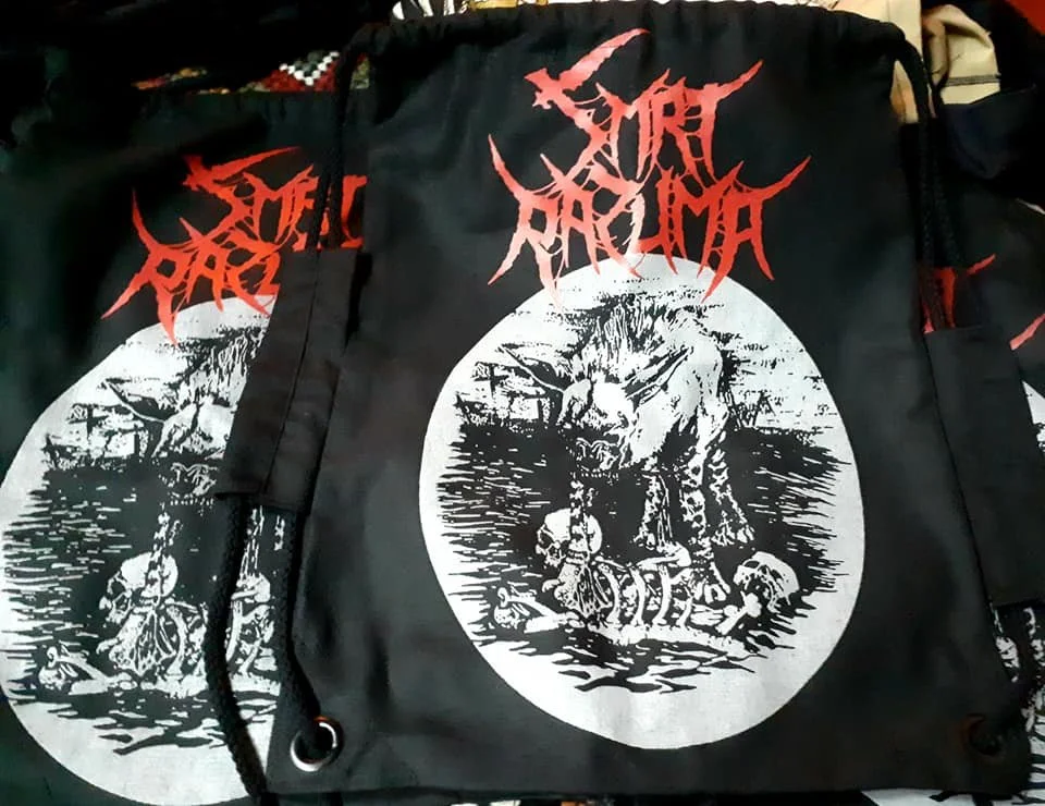 Black drawstring bag with red band logo and artwork depicting a monstrous creature and skeletons, associated with metal or death metal music.