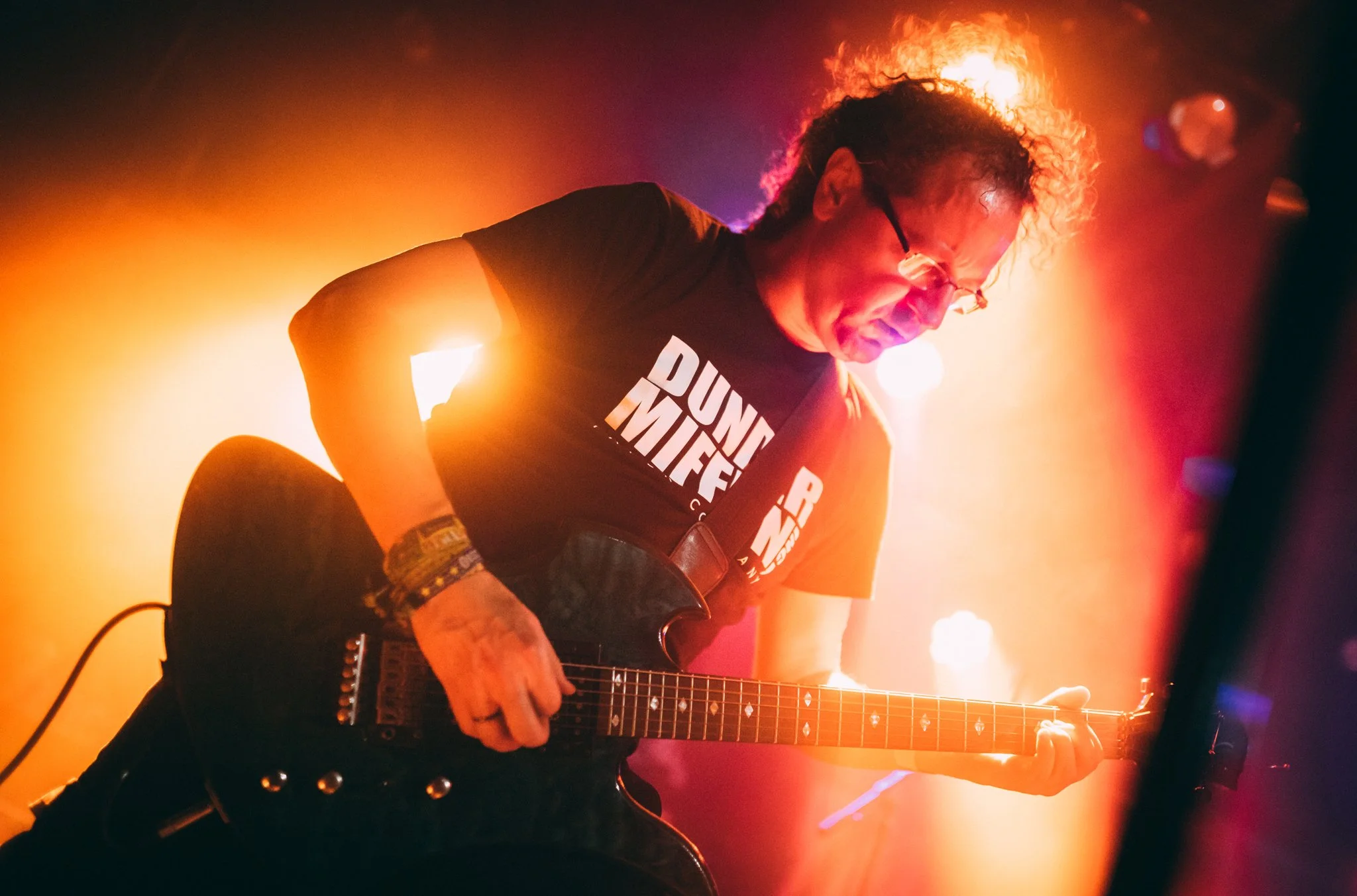 A musician with curly hair, glasses, wearing a black "