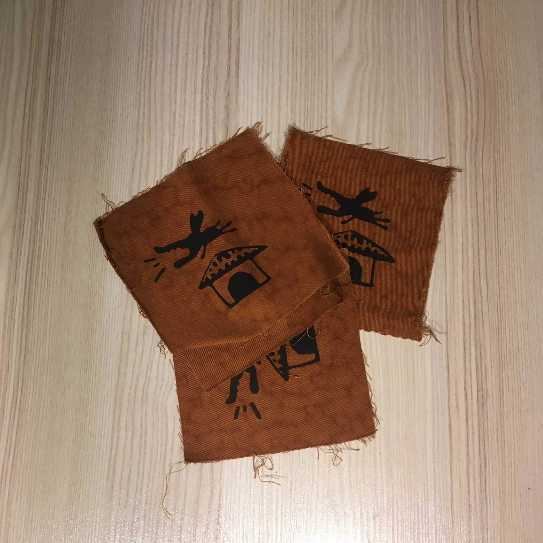 Two torn orange fabric pieces with black printed deer and tree silhouettes on a light wooden surface.