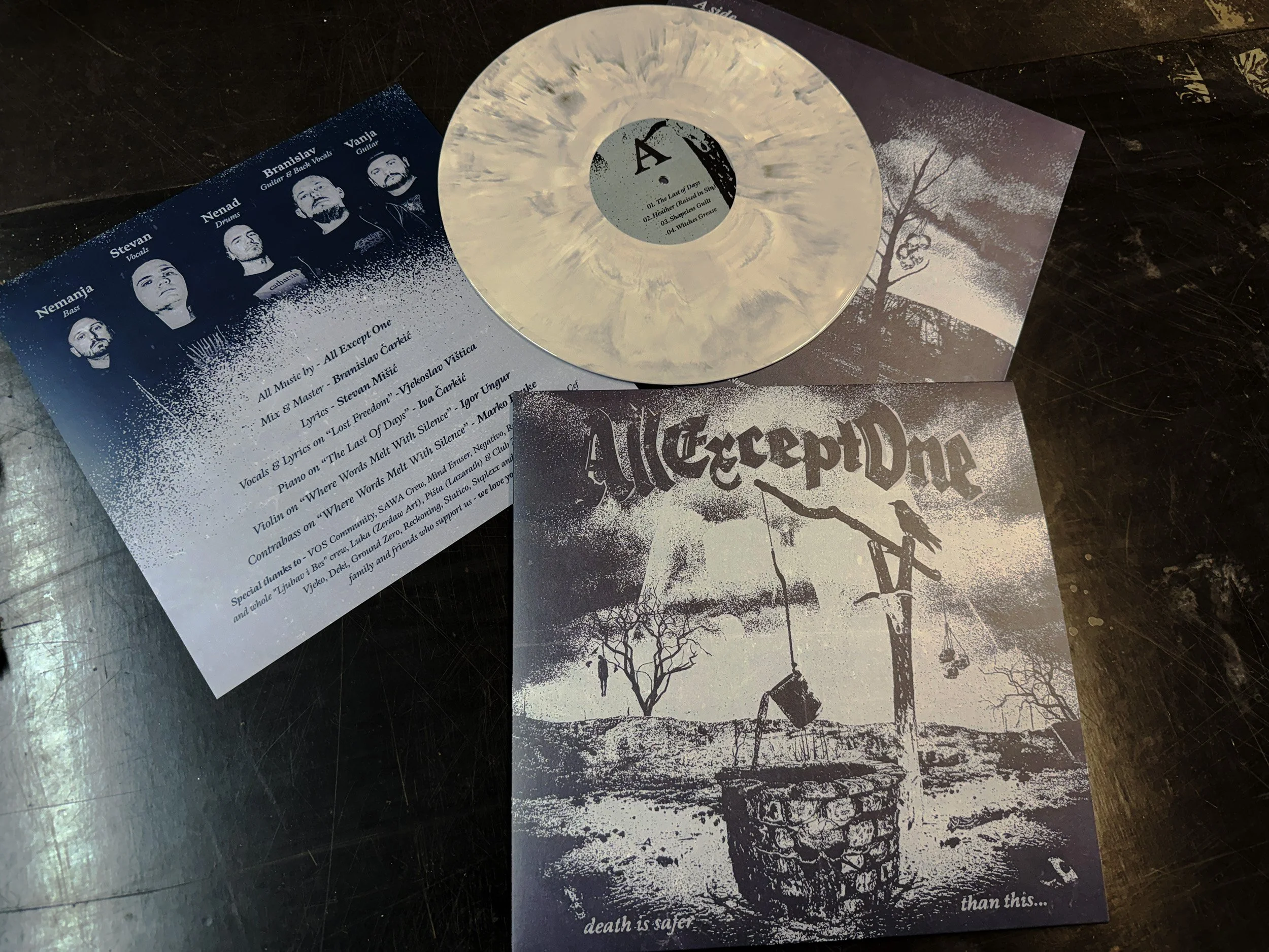 A vinyl record and album cover with a black and white tree and figure silhouette, along with promotional materials including band photos and song list.
