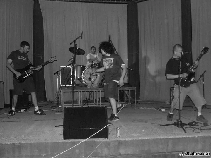 Group of four young musicians performing on stage with drums, guitars, and microphones.