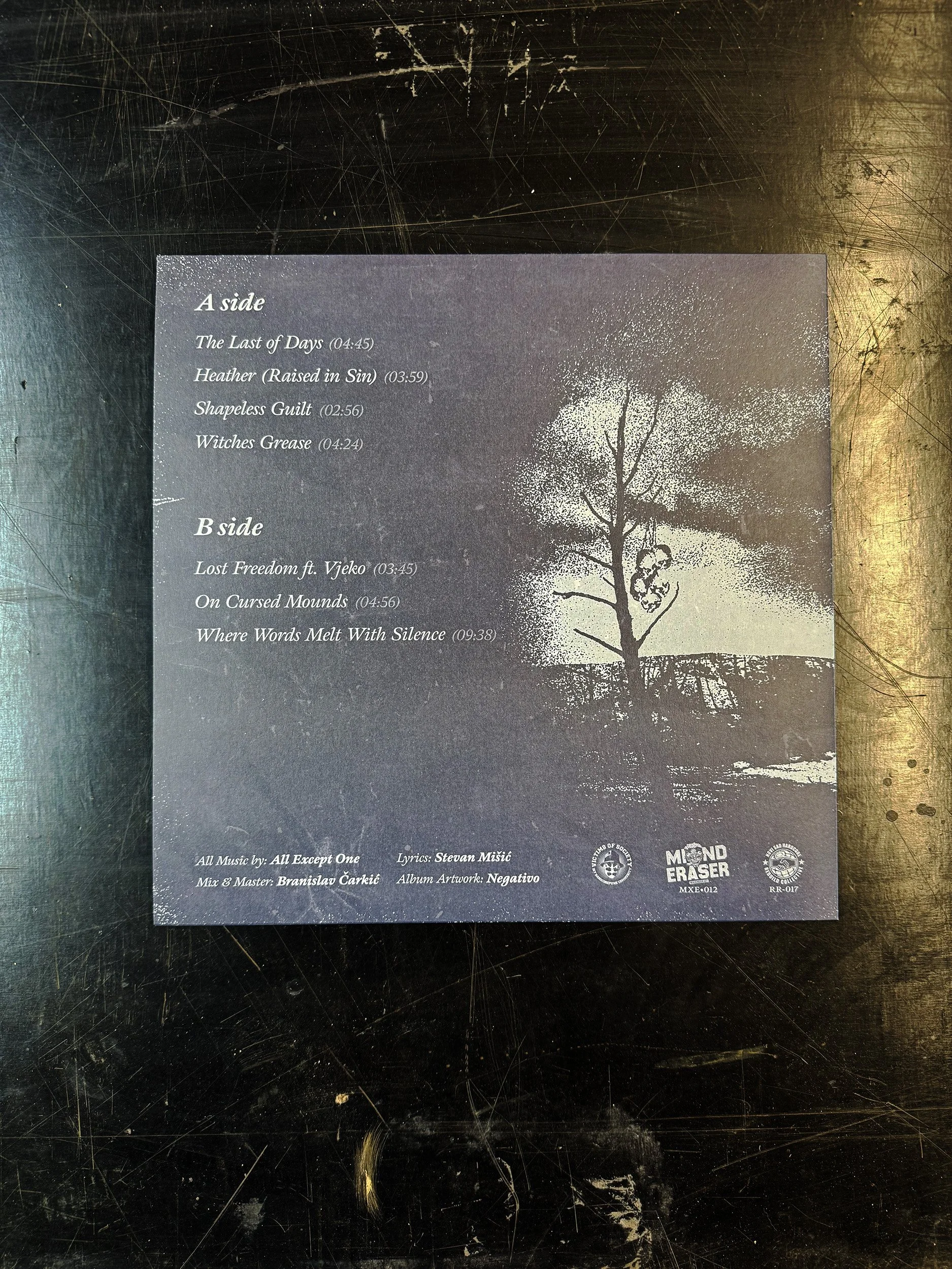 Back cover of a music record album with a dark background, white text listing song titles and credits, a silhouette of a tree, and logos at the bottom.