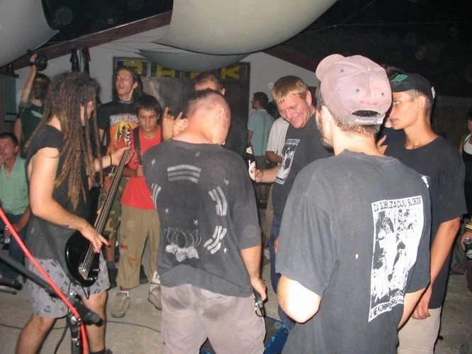 Group of young people dancing and socializing at a concert or party, with one person playing guitar.