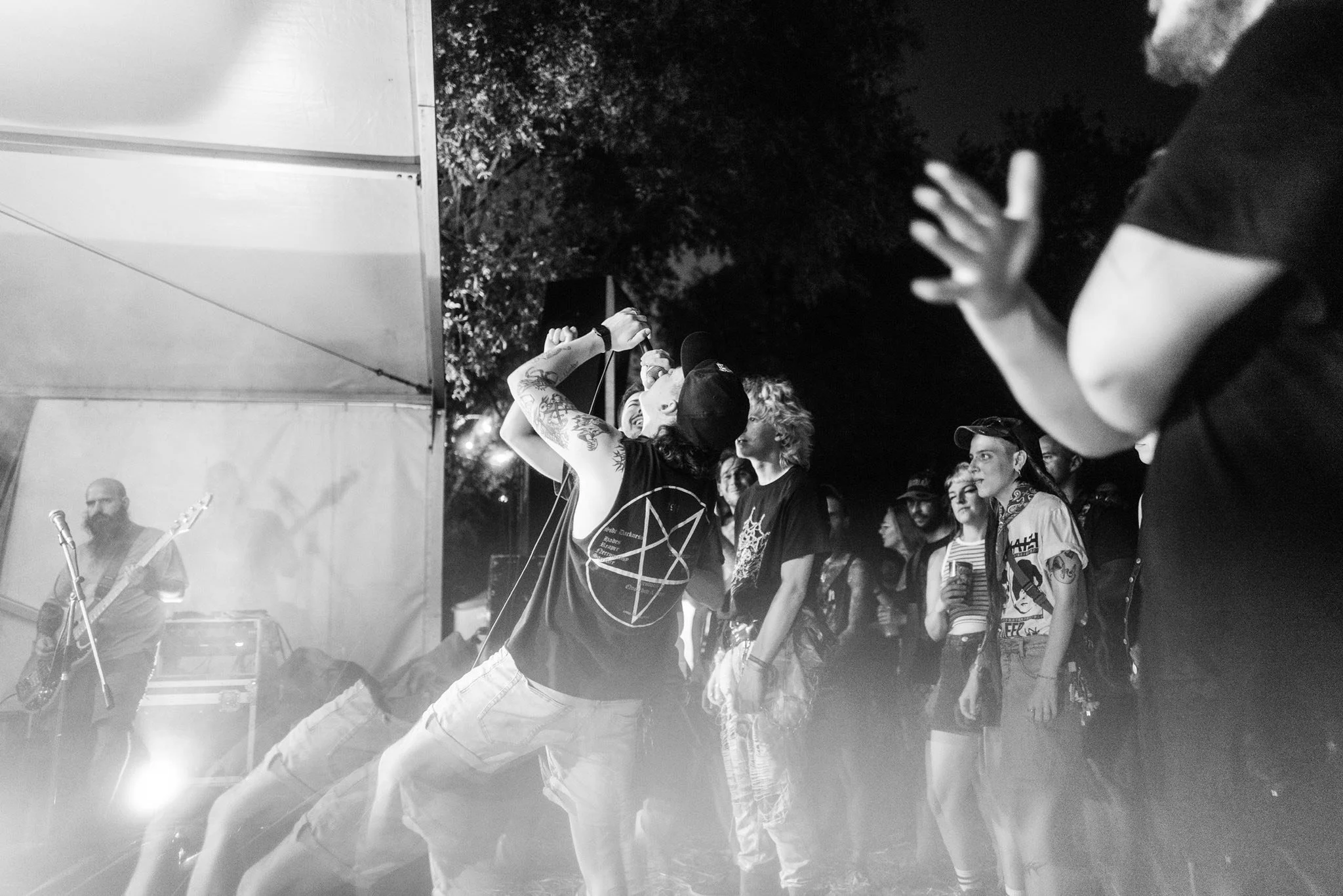 A black and white photo of a crowd at a concert or festival, with a singer holding a microphone on stage and audience members watching attentively.