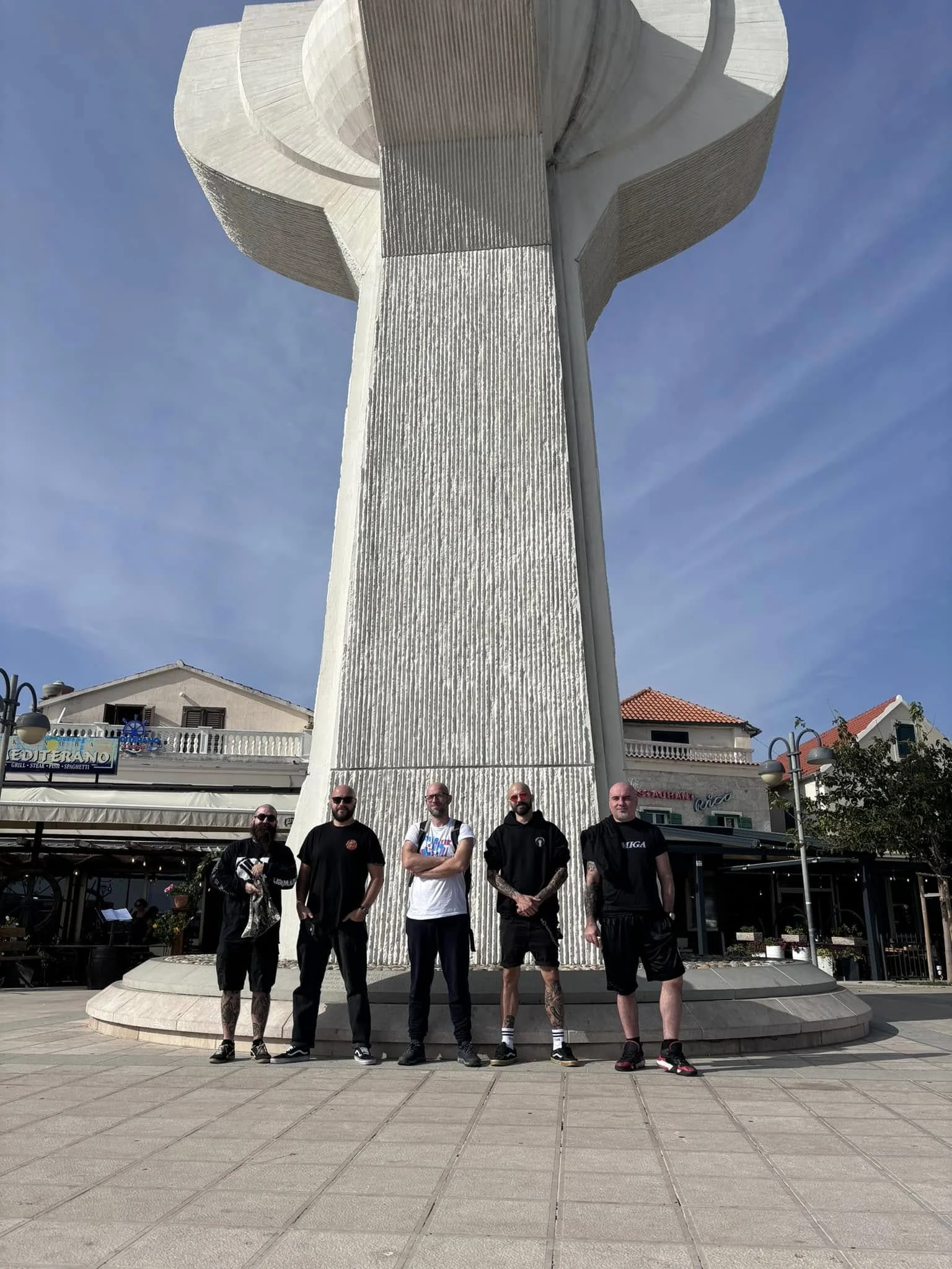 Group of five men standing in front of a large white monument in an outdoor plaza.
