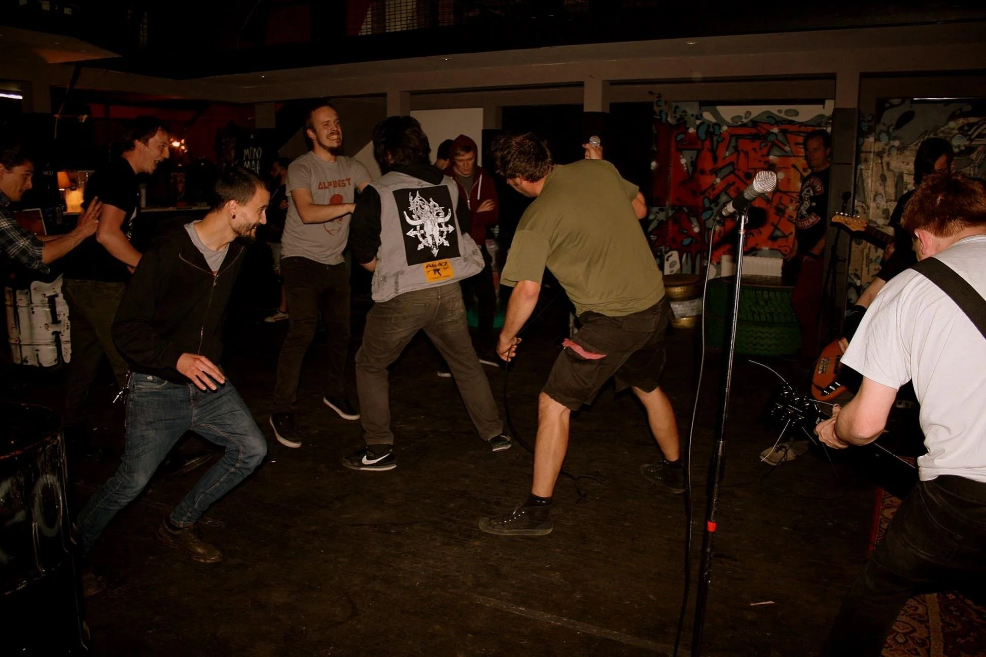 People dancing and having fun indoors at a music event, with some playing musical instruments and a microphone visible in the scene.