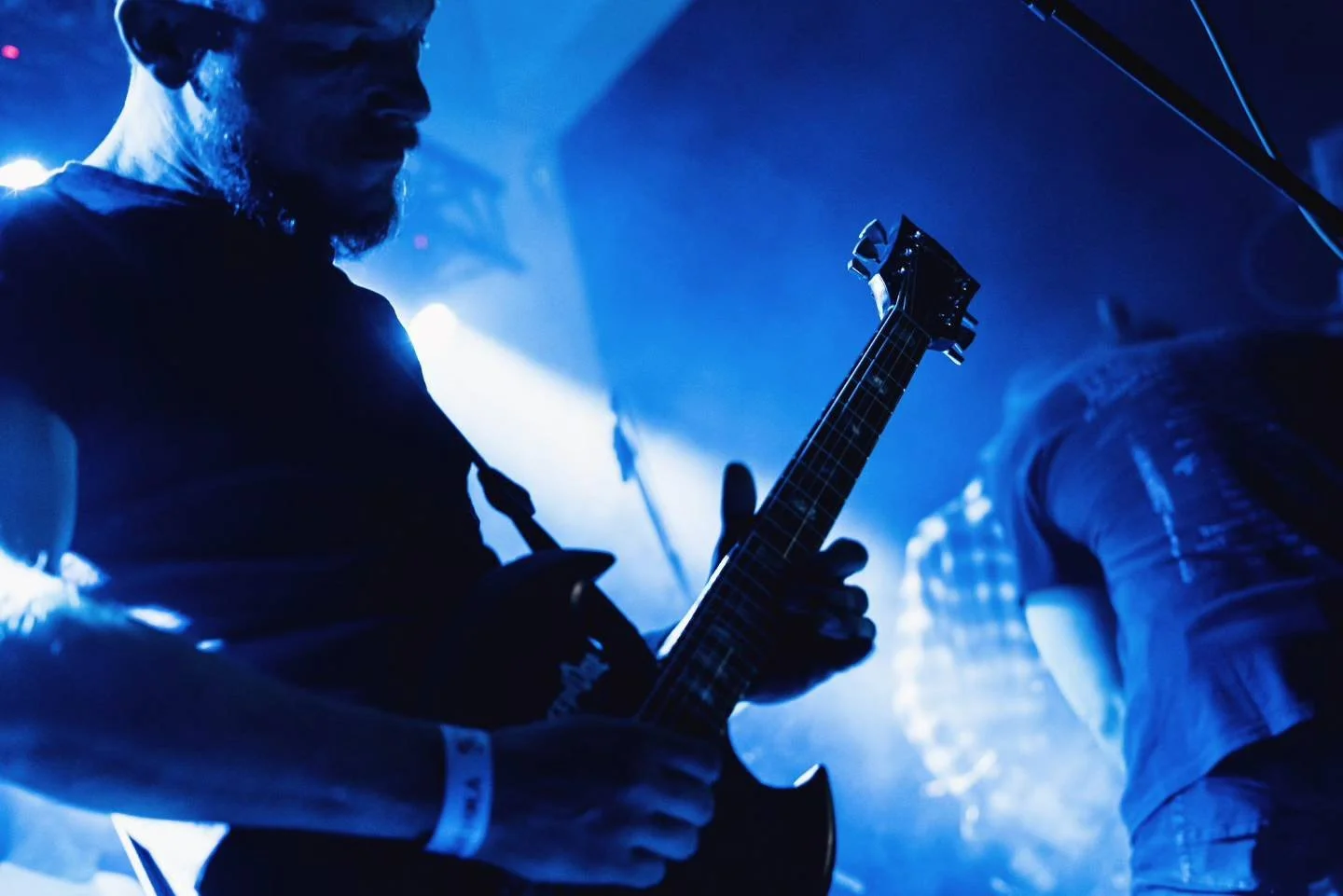 Person playing electric guitar on stage with blue lighting at a concert or live music event.