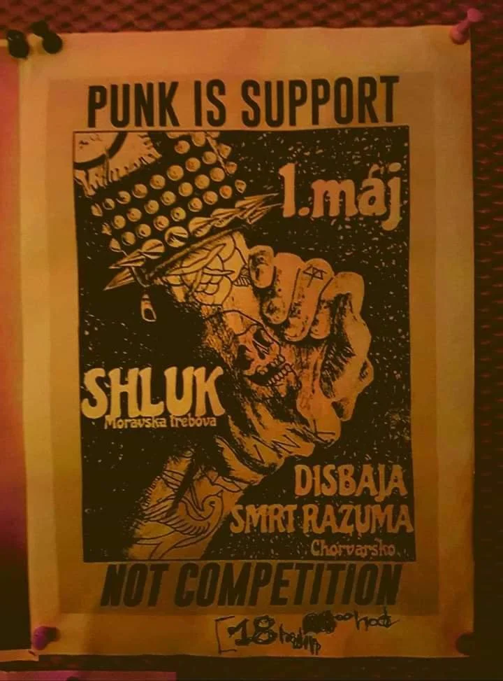 A protest poster with a black and orange graphic design. It features a clenched fist holding a skull with a poppy flower, and a skull with a large knife. The text reads 'Punk is Support 1. maj', 