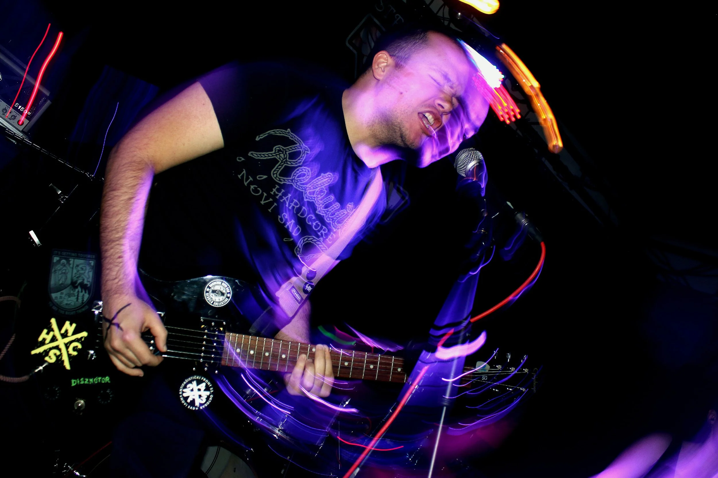 A musician performing with a guitar in a dark setting, colorful lights creating motion effects.
