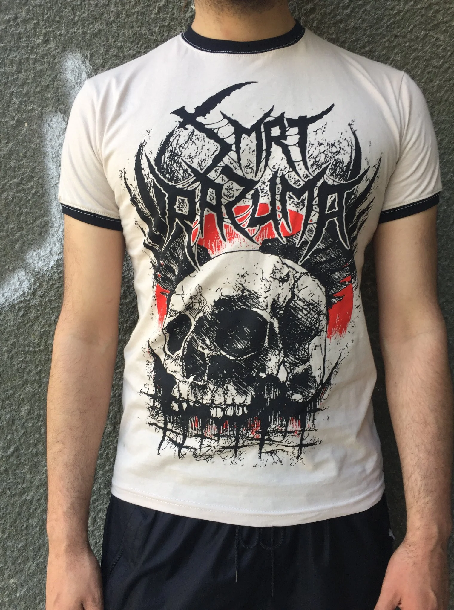 Person wearing a white graphic t-shirt with black and red design, standing against a dark textured wall.