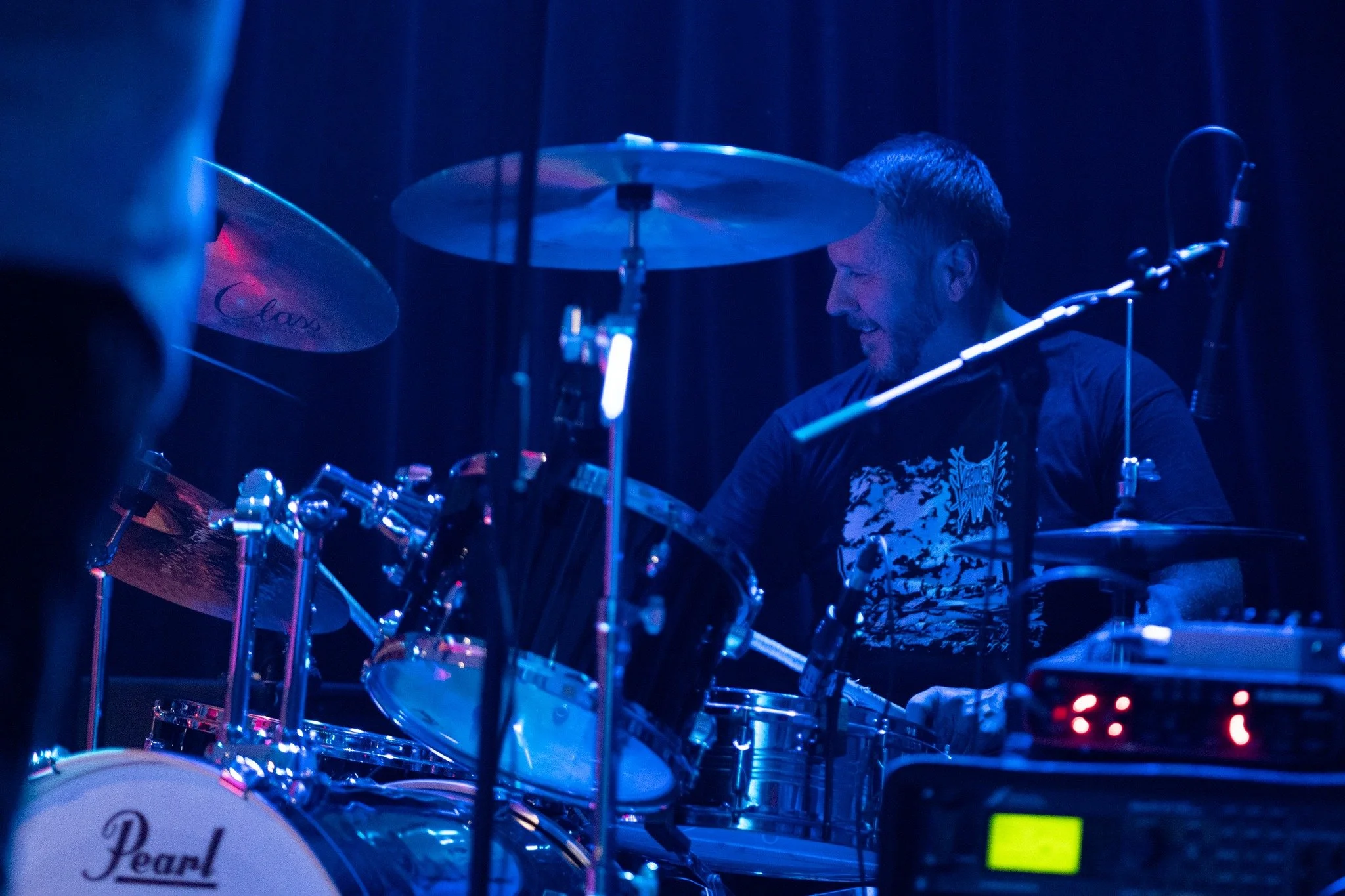 A drummer playing a drum set on stage under blue and purple lighting.