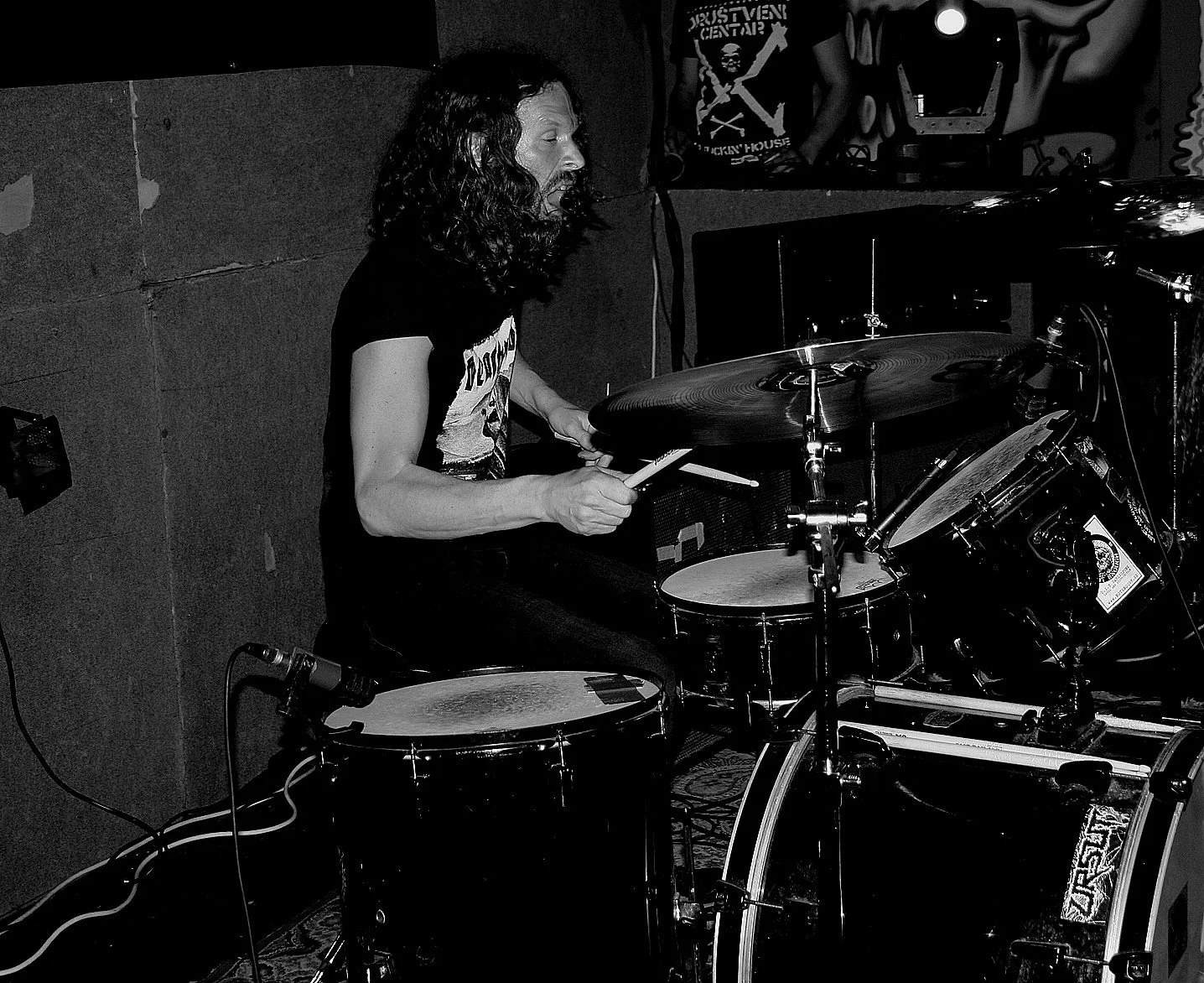 Black and white photo of a musician playing drums in a recording studio, with a microphone positioned near the snare drum.