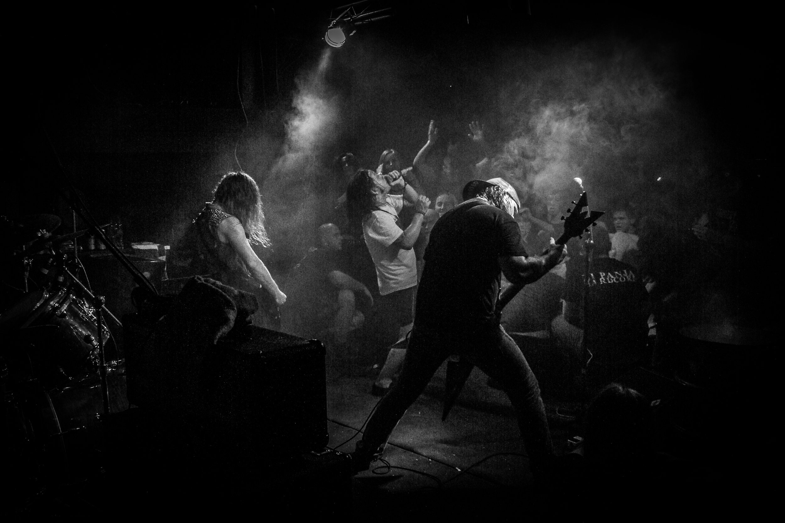 A black and white photo of a live music performance on stage with a band and audience, with smoky atmosphere and dramatic lighting.
