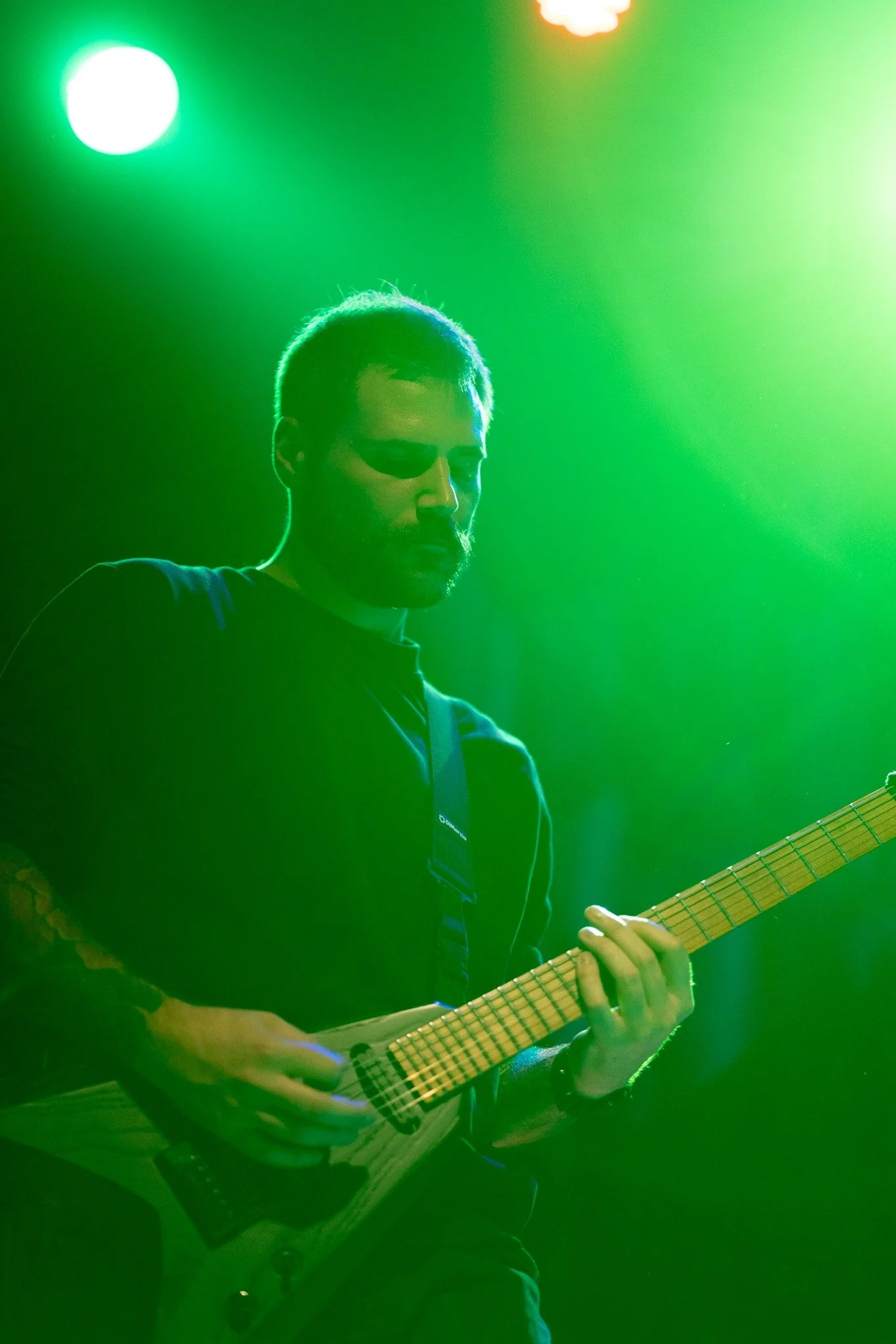 A man playing an electric guitar on stage, illuminated by green lighting.