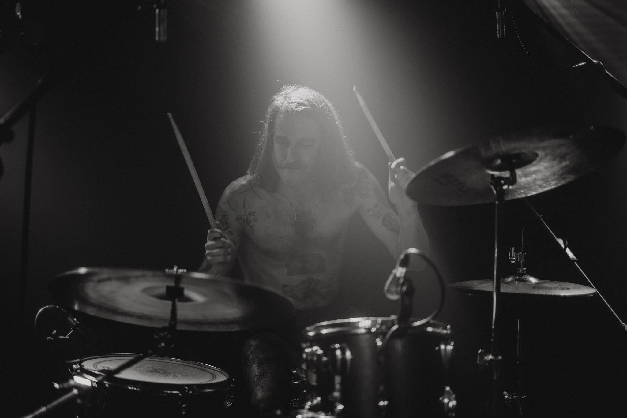 Black and white photo of a male drummer playing a drum set, with a spotlight shining down from above.