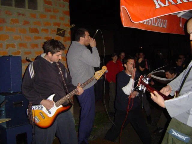 A group of young men performing with musical instruments outdoors at night, with a crowd watching.