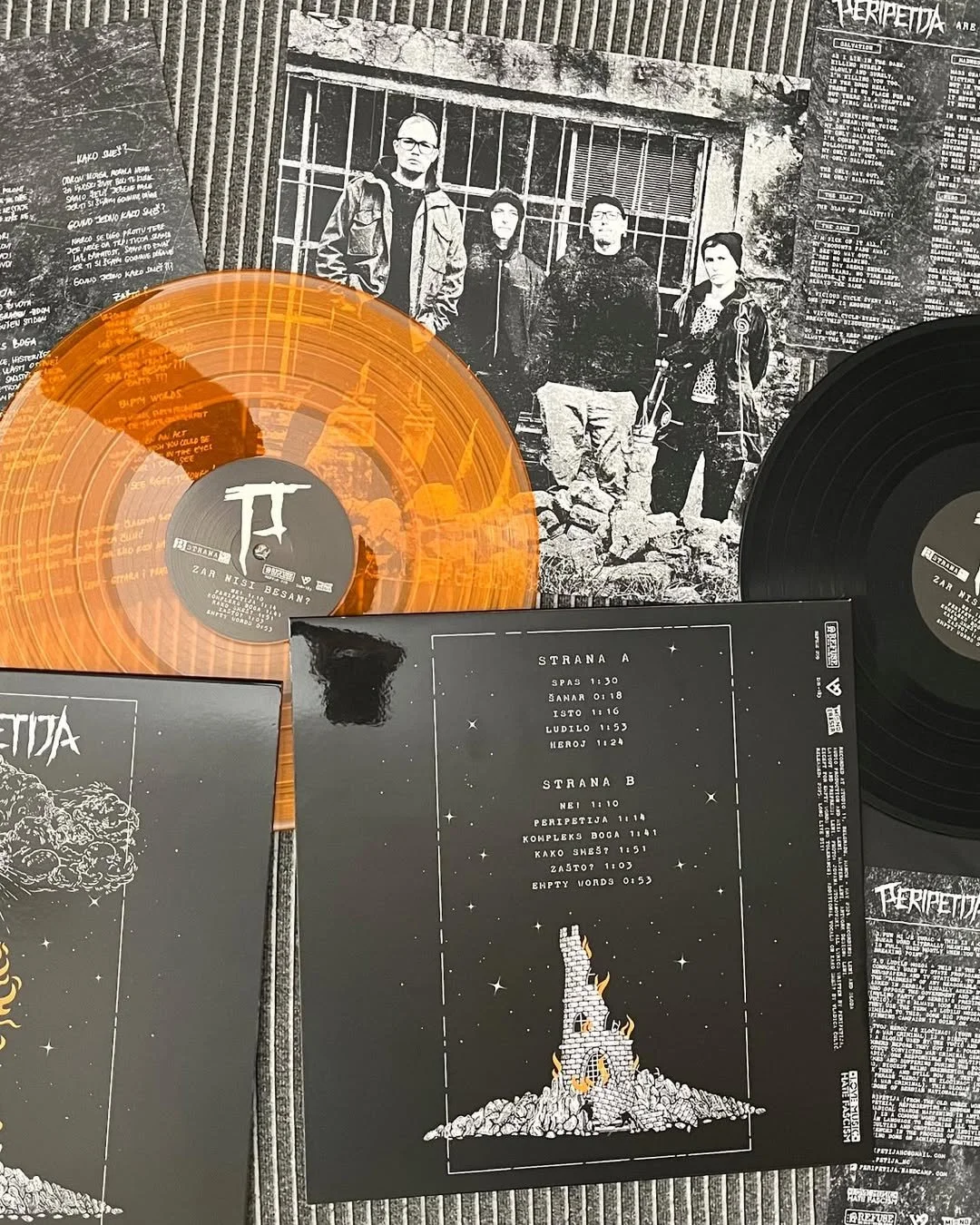 A collection of vinyl records and album covers on a table, with a black-and-white photograph of four people in front of a barred window in the background. The records are orange and black, with one partially visible, and the album covers display vari