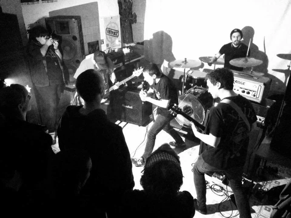 A band playing live music in a small indoor venue with an audience watching