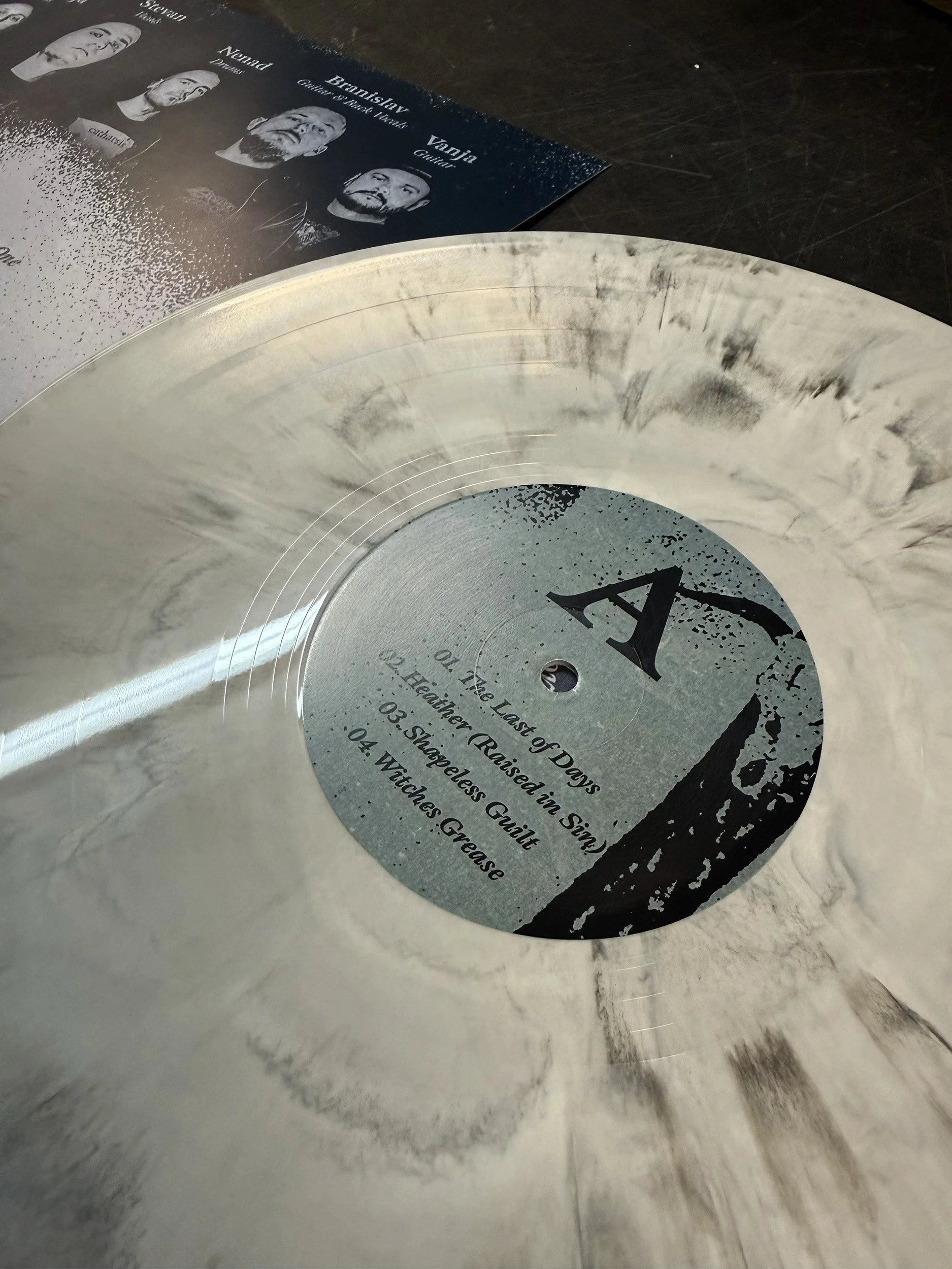 Close-up of a vinyl record with a partially visible album cover in the background, showing four black and white portraits of band members.