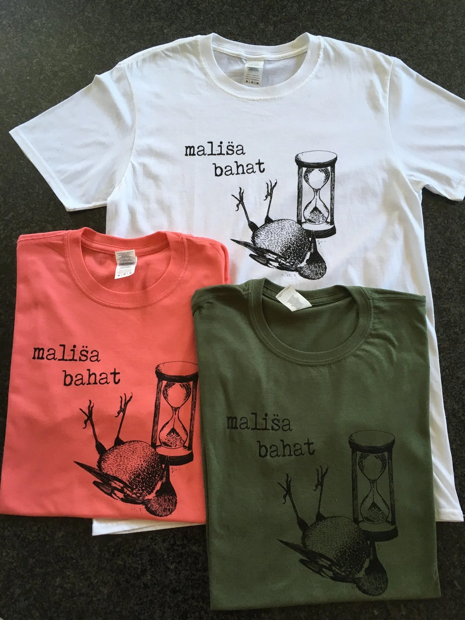 Three T-shirts in white, coral, and olive green, each featuring a black graphic of a beet, an hourglass, and the text "mališa bahat".