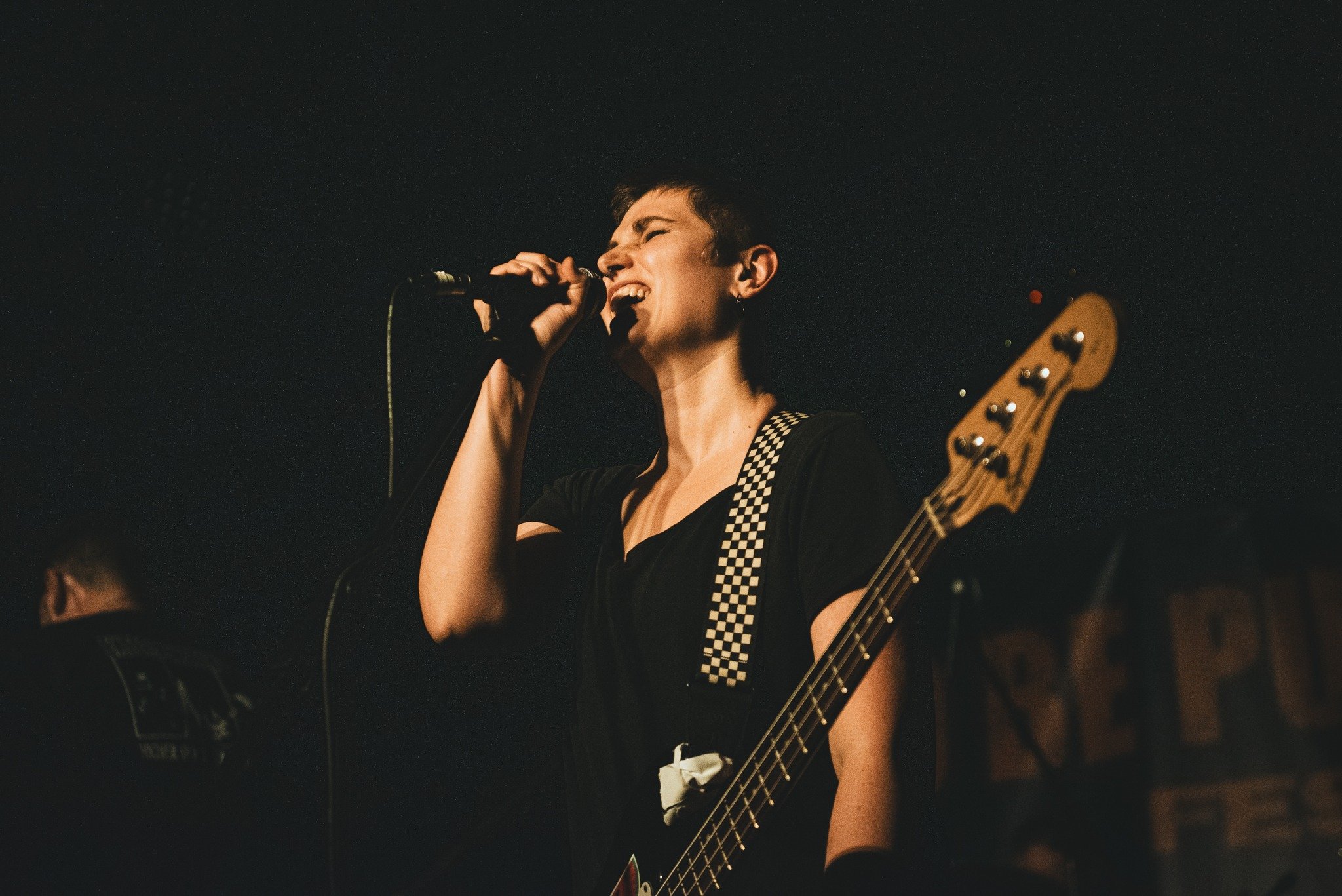 A woman singing into a microphone while playing a guitar on stage in a dark setting.