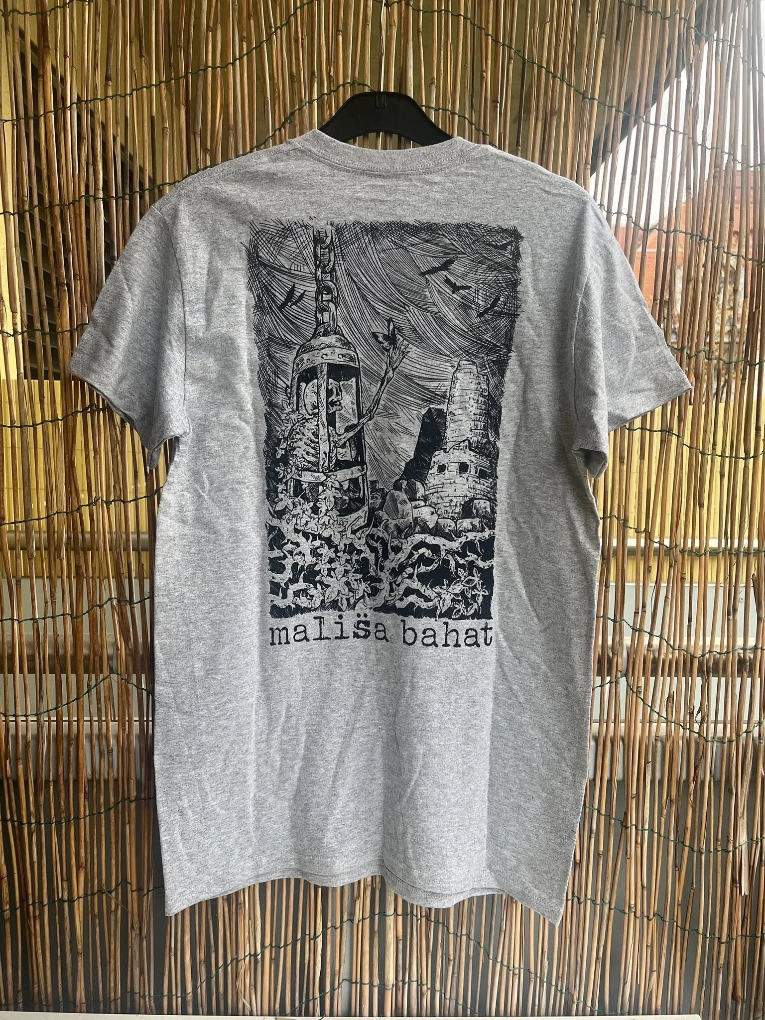 Gray T-shirt with black graphic design featuring a soldier with a helmet, surrounded by leaves, a castle tower, and birds, with the text 'malissa bahat' at the bottom.