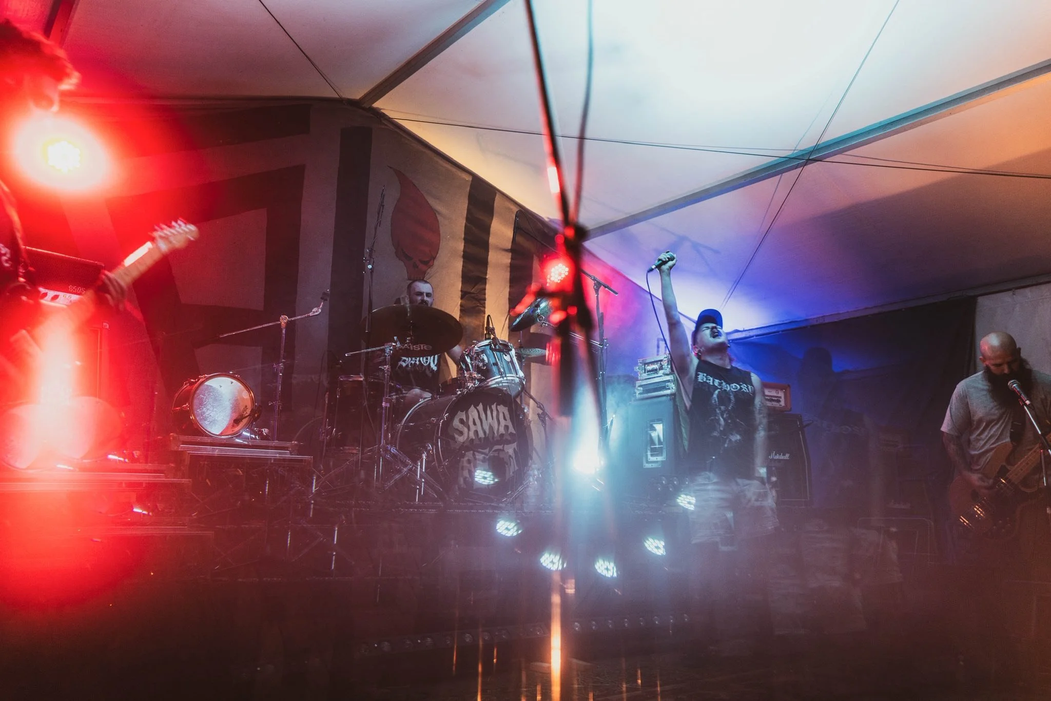 A band performing on stage with colorful lights, a drummer, a vocalist raising their fist, and other musicians including guitarists.