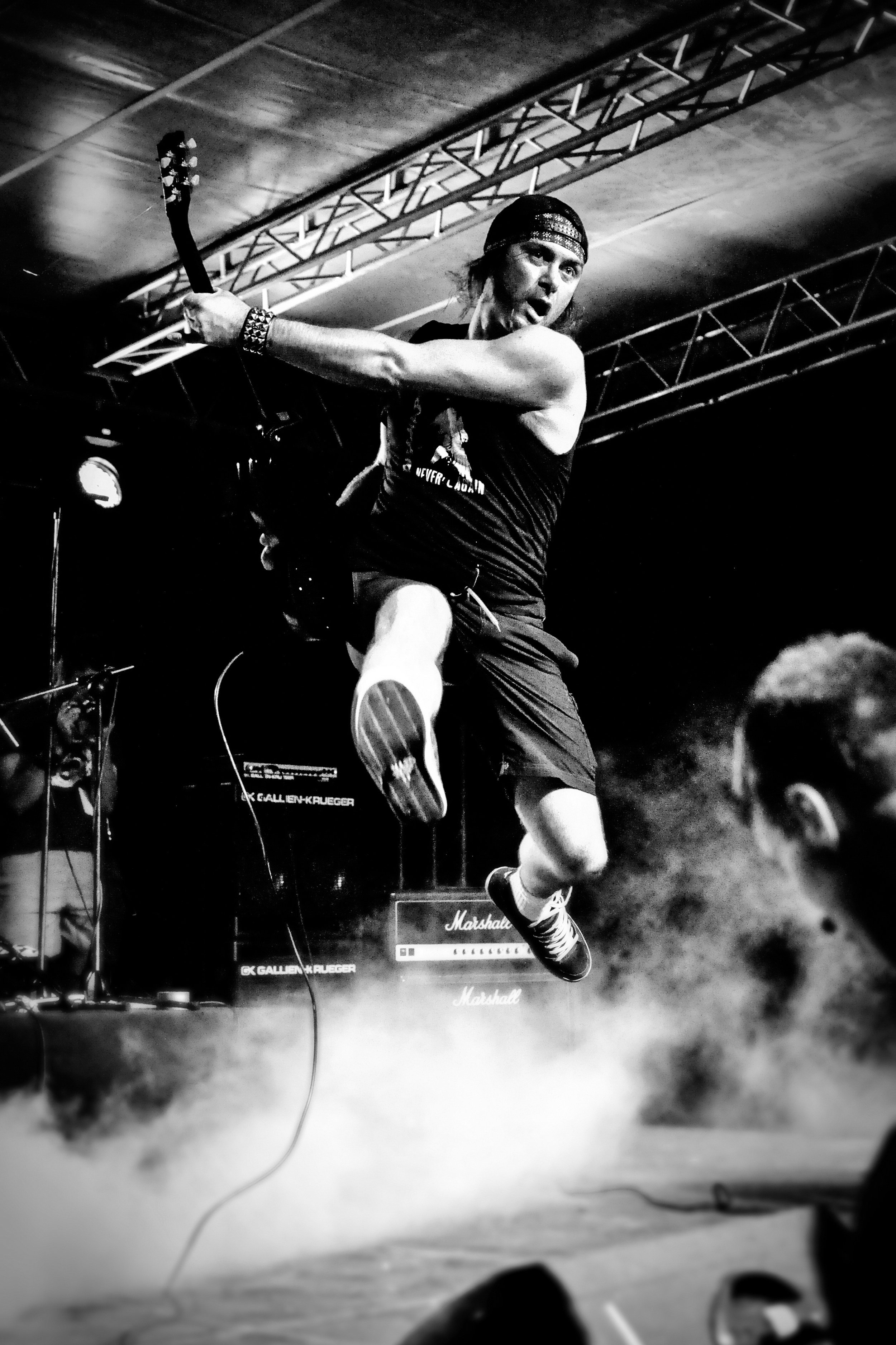 A musician jumping on stage playing guitar, with musical equipment and fog effects in the background. Band name: VitaminX