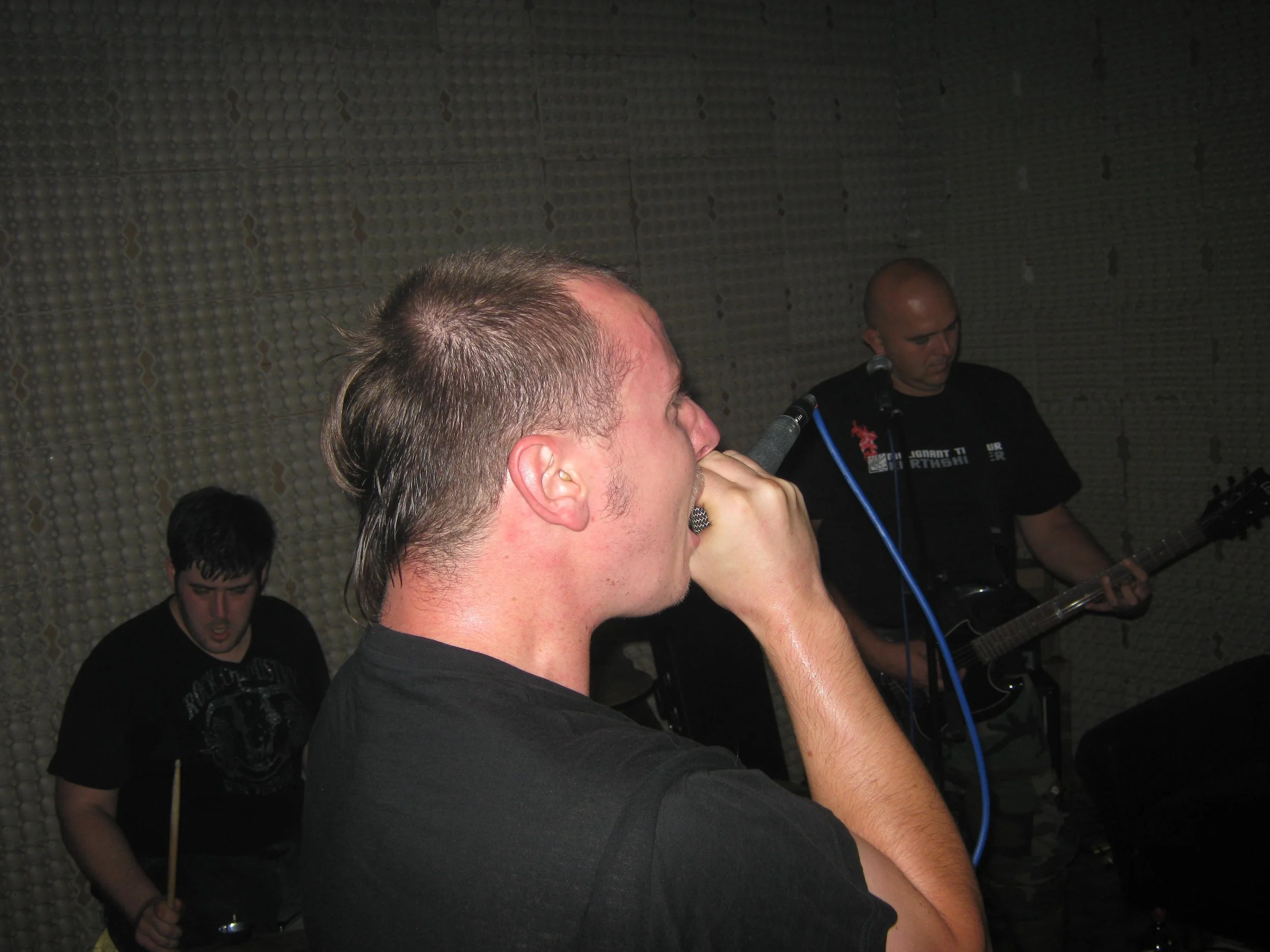 Close-up of a person singing into a microphone with a group of musicians in the background.