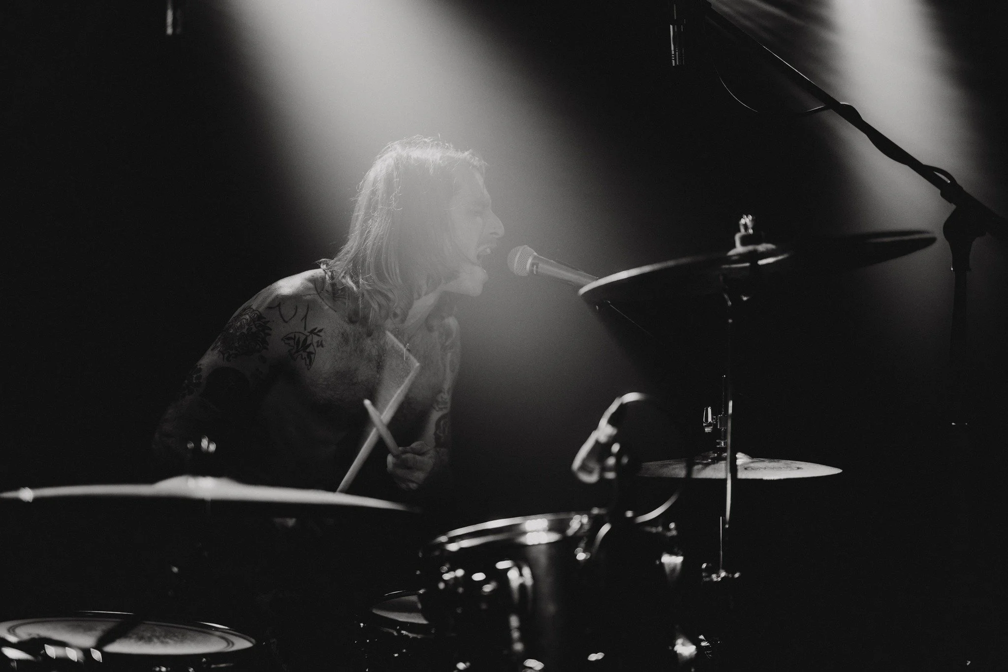 A black and white photo of a woman with long hair singing into a microphone while playing a grand piano, with dramatic lighting focusing on her face.