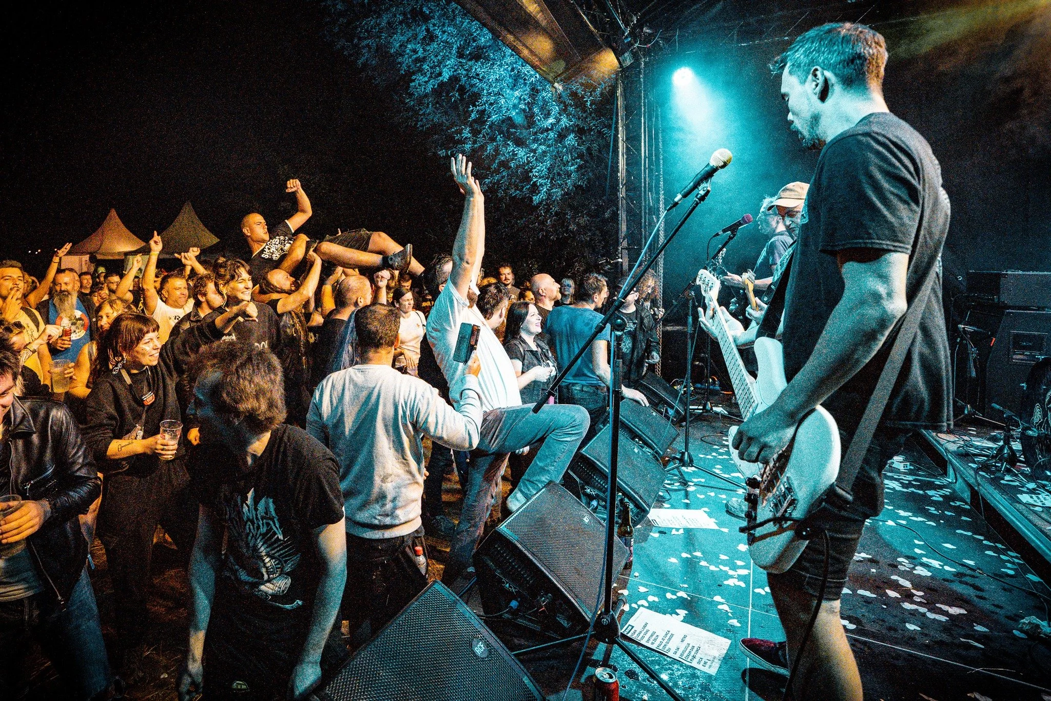Band performing on stage at night with the audience watching and cheering, some raising their hands, and a crowd surfing crowd member.