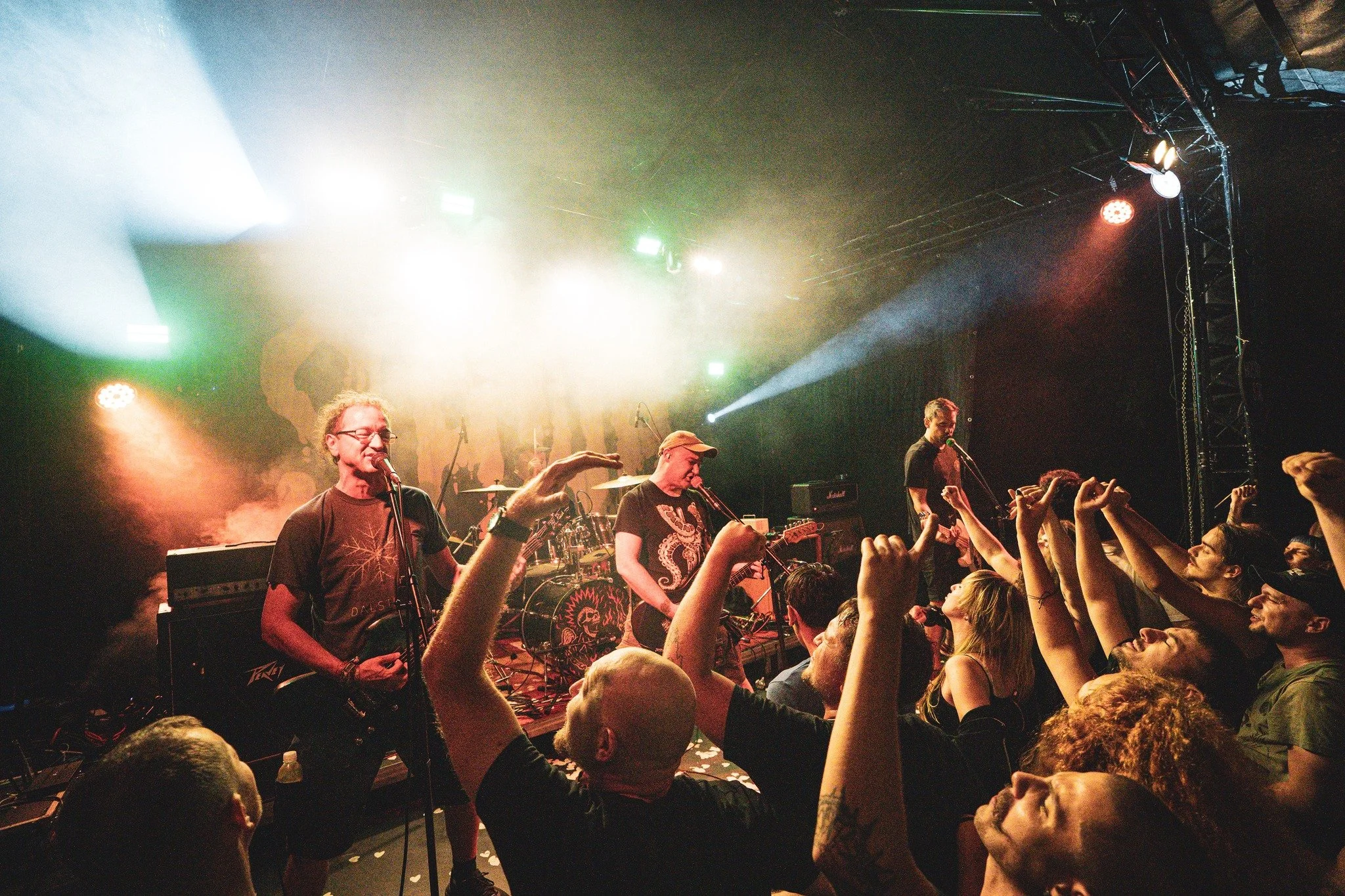 A live concert with a band performing on stage in front of a crowd, stage lights shining brightly and audience members raising their hands.