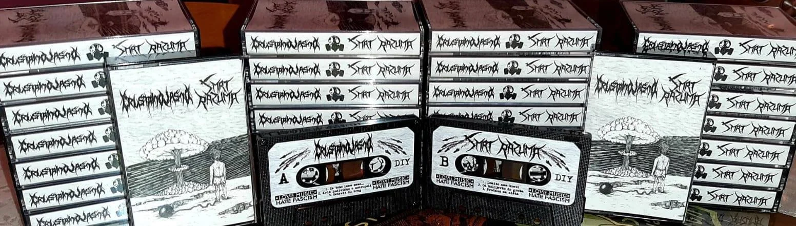 A collection of cassette tapes and boxes of the album titled 'Smrt Razuma.' The album cover features a drawing of a person standing on the beach watching a nuclear explosion in the distance, with a mushroom cloud and a bomb in the foreground.