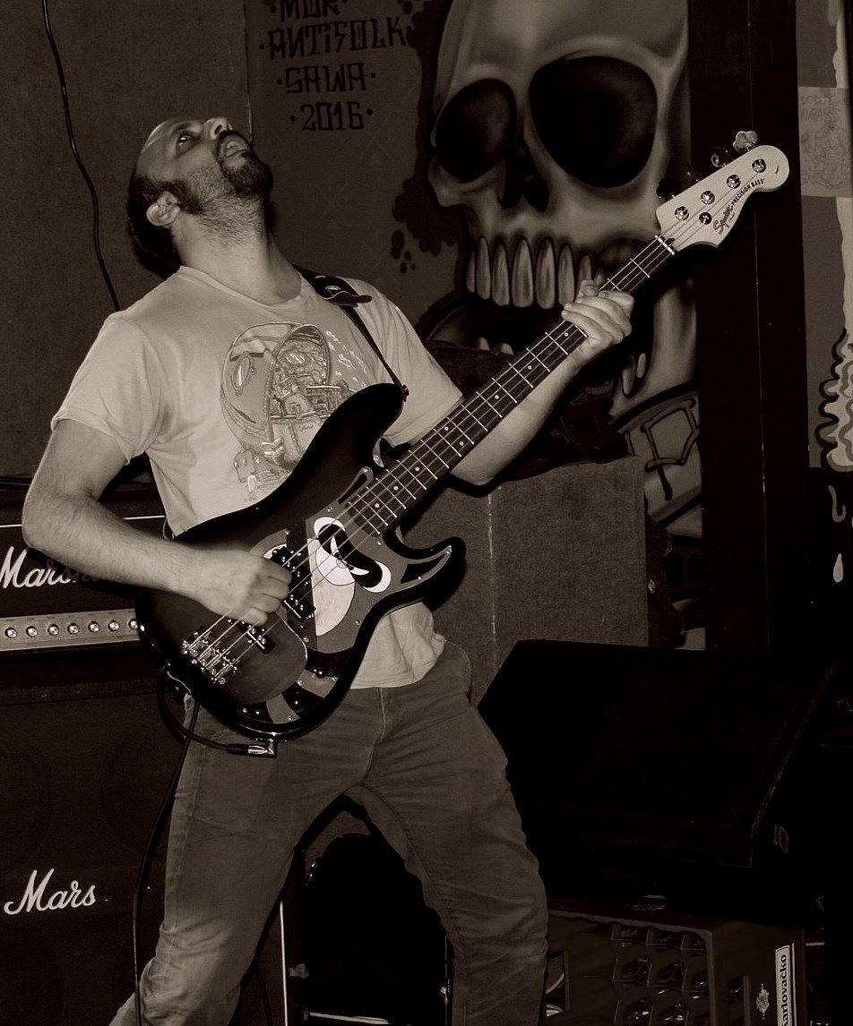 A man playing an electric guitar on stage with a mural of a skull in the background.