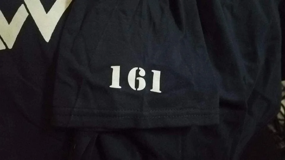 Close-up of a black shirt or jacket with the number '161' printed in white.