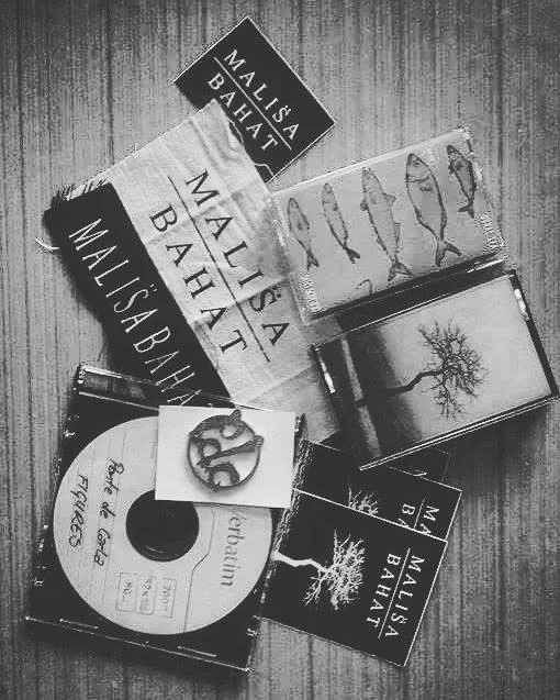 Books, a CD, and a small decorative item on a wooden surface. The CD "Malisa Bahat" includes a cover featuring trees and abstract designs.