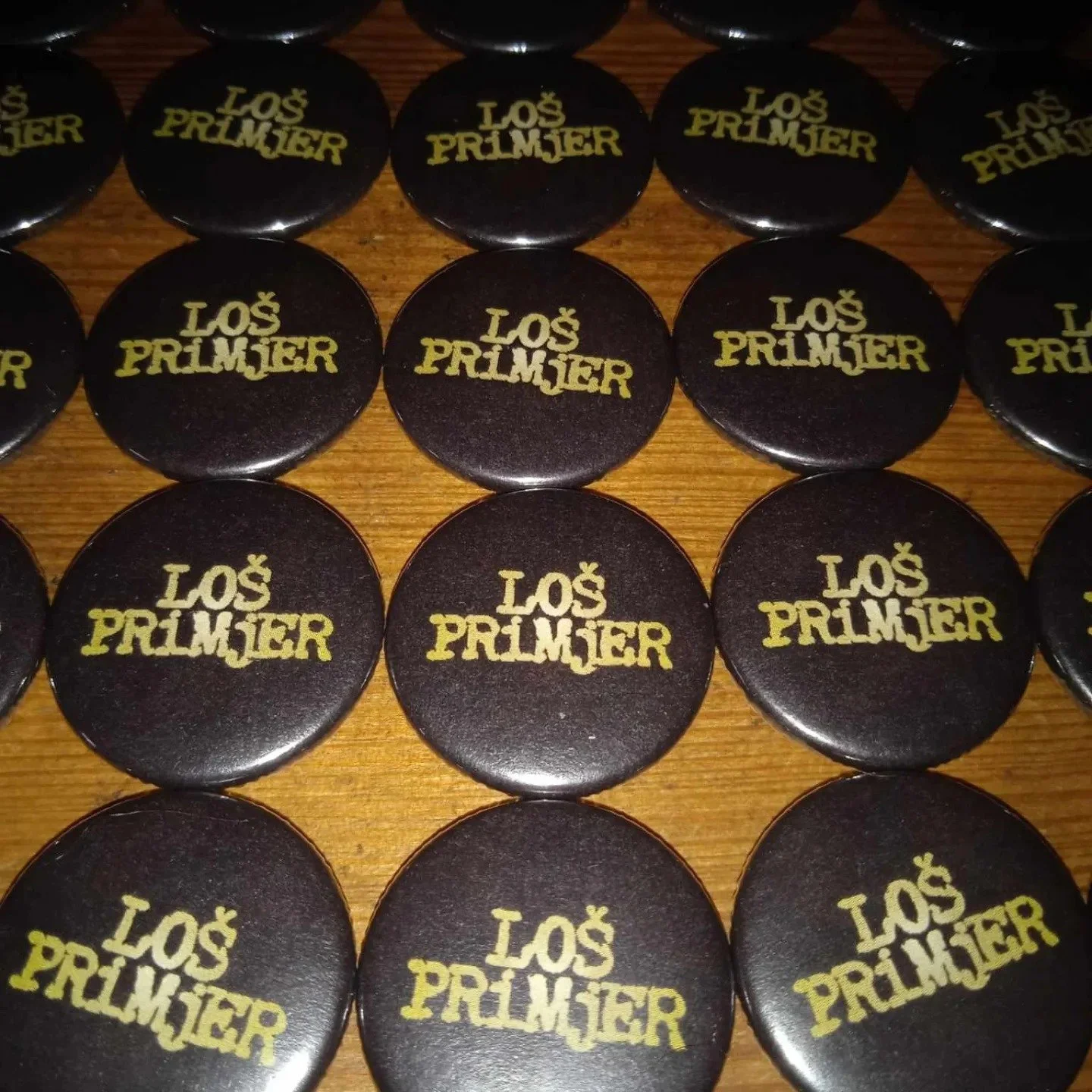 Collection of round black badges with gold text saying 'LOS PRIMJER' arranged on a wooden surface.