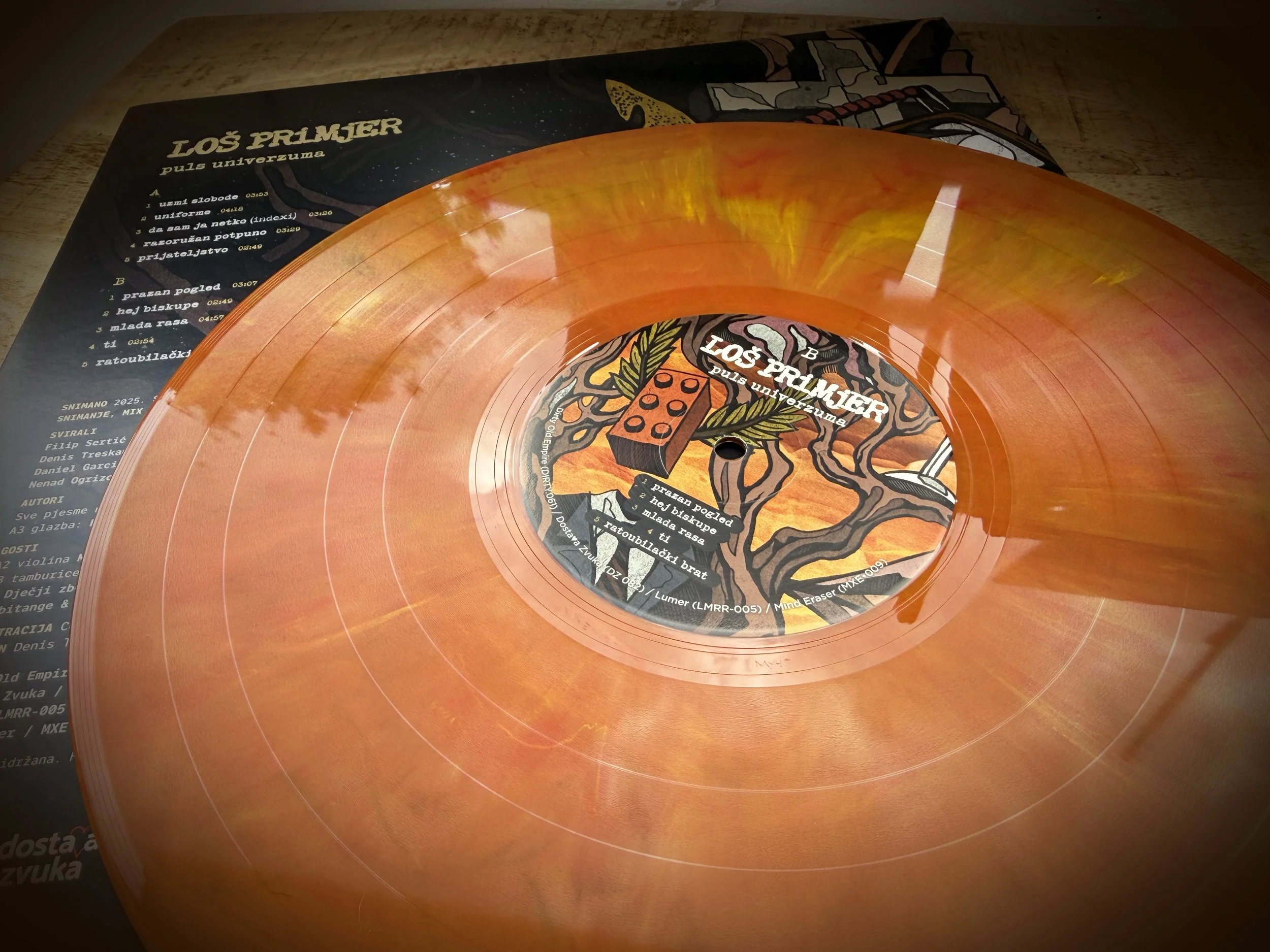 Orange vinyl record with a colorful label on a light-colored wooden surface.