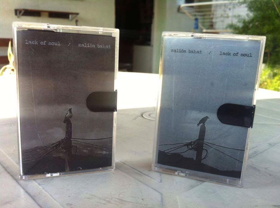 Two cassette tape cases, one black and one blue, with the same artwork of a person standing on a street corner at night, holding a dog, with the song title 'Lack of Soul' and artist 'Malisa Bahat' written at the top.