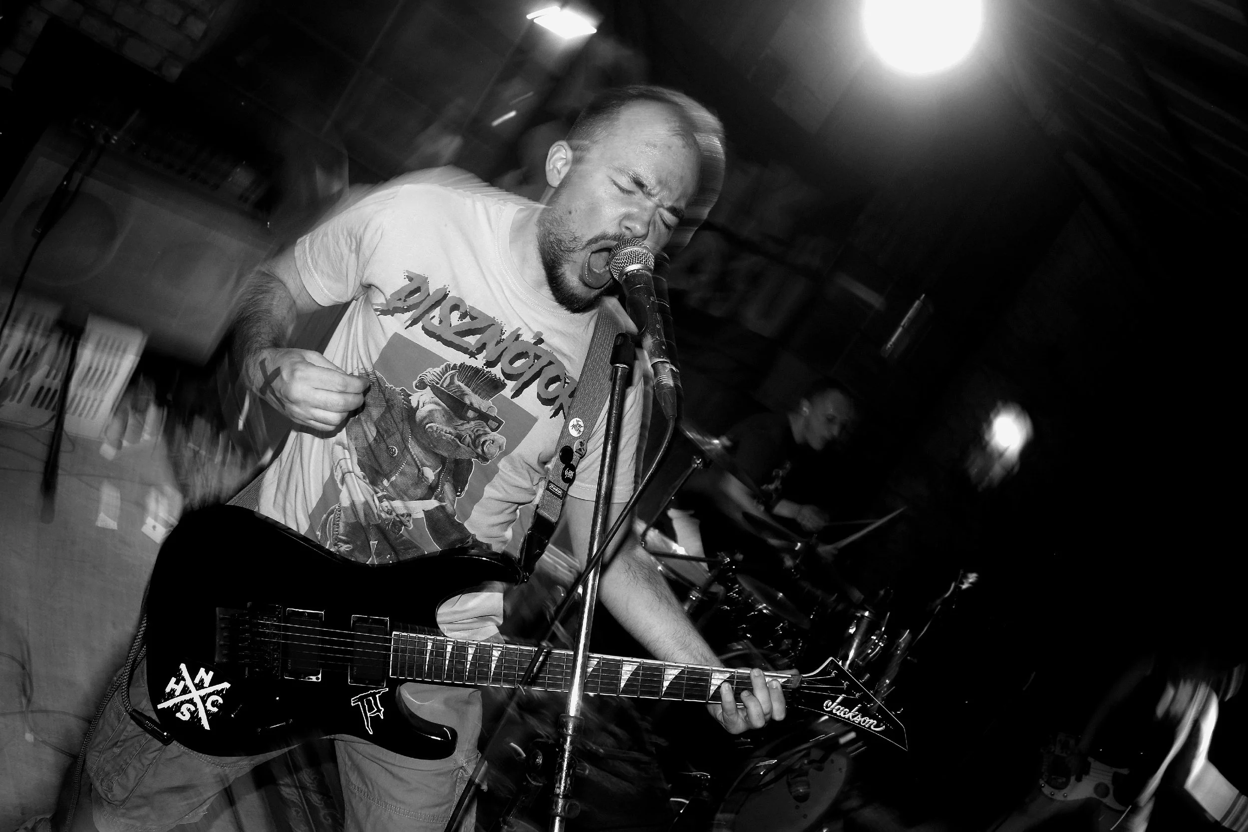 A man singing into a microphone while playing an electric guitar at a live music venue.