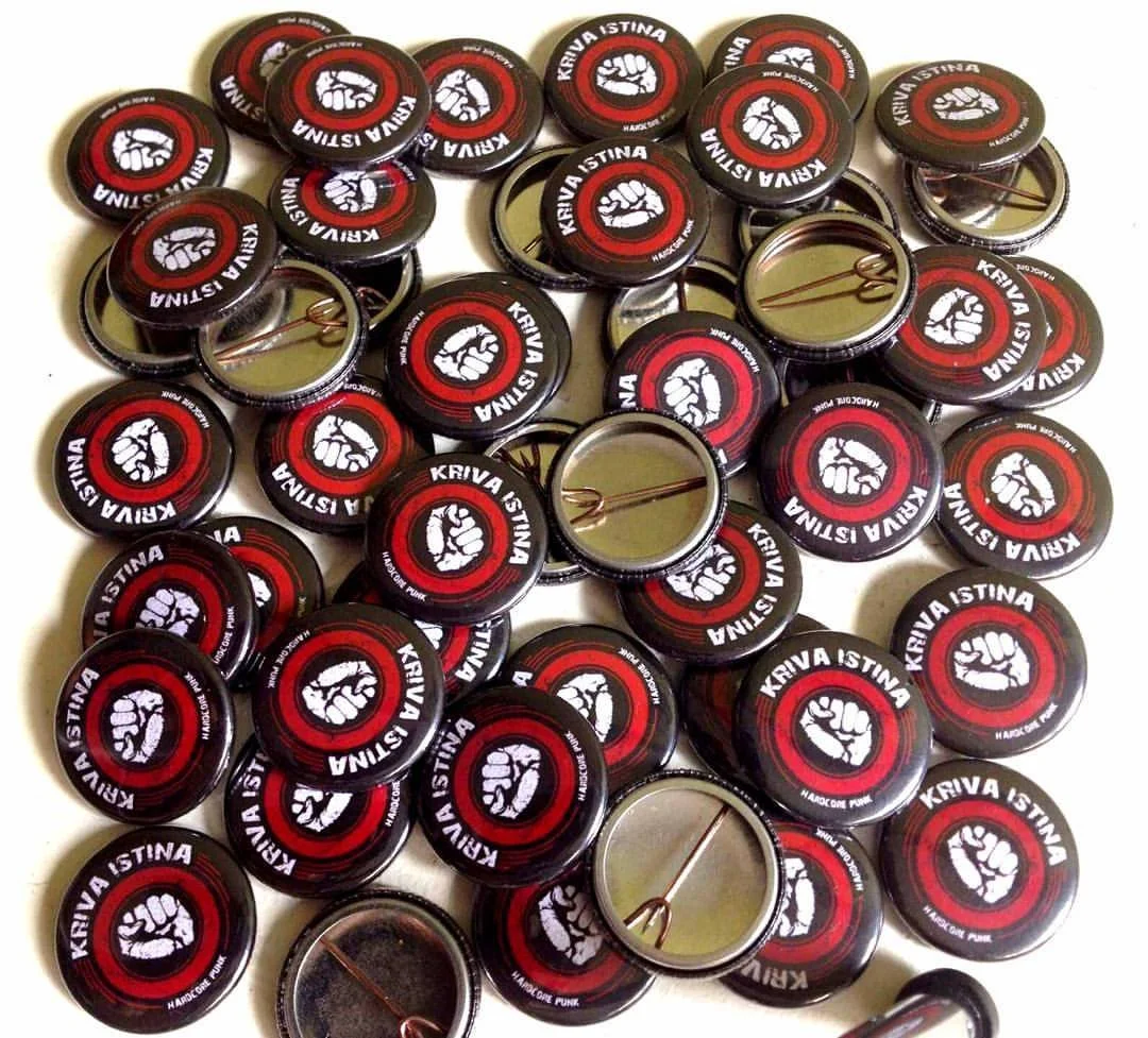 A collection of black metal pin badges with a red circle and a white clenched fist logo, and the words "Kriva Istina" and "Hardcore Punk" printed on them.