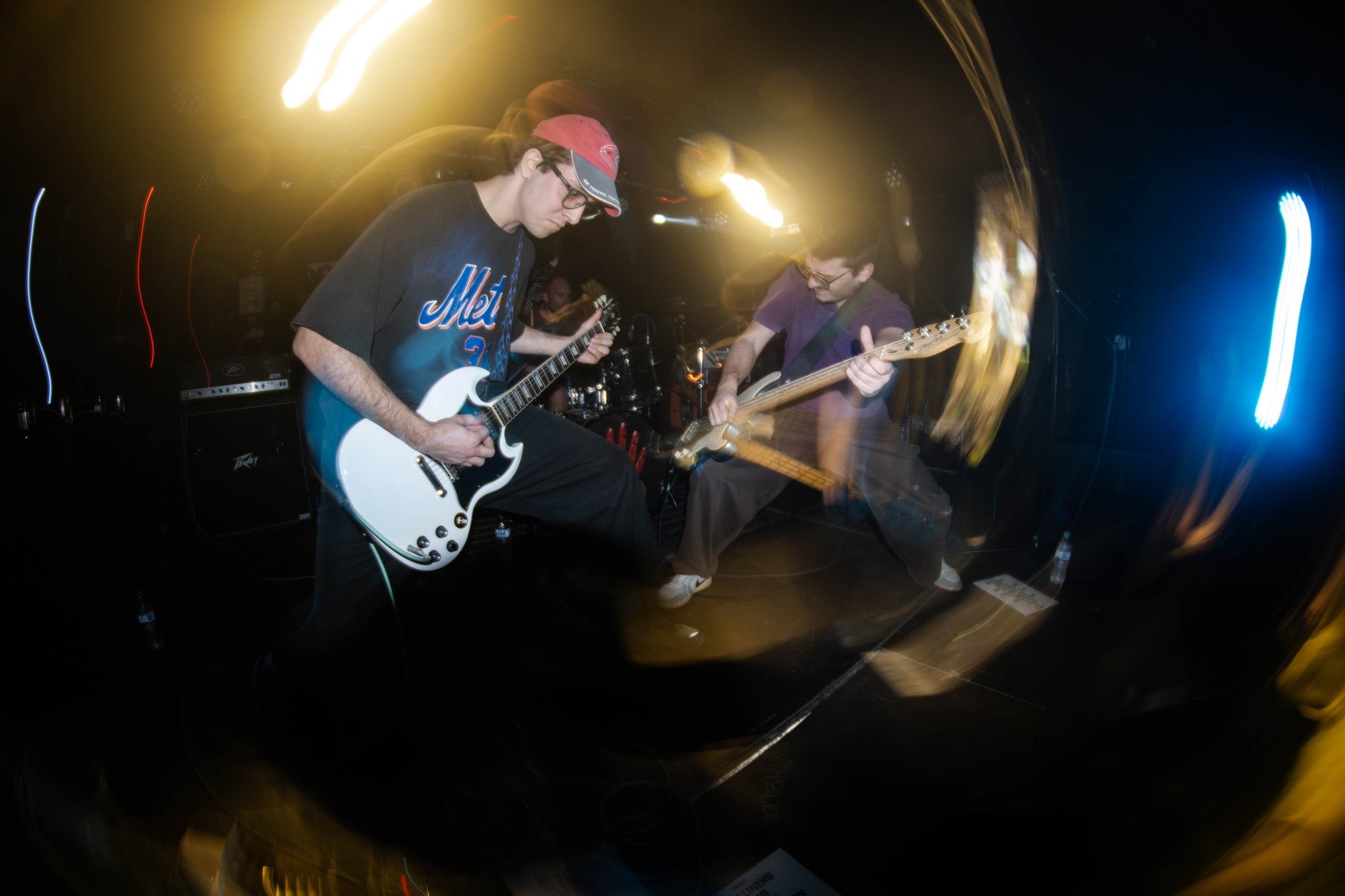 Two young men playing electric guitars on stage during a live music performance with colorful stage lights and motion blur.