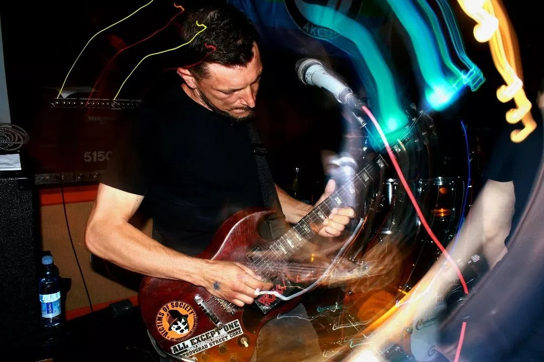 Man playing electric guitar on stage with colorful light trails in the background.