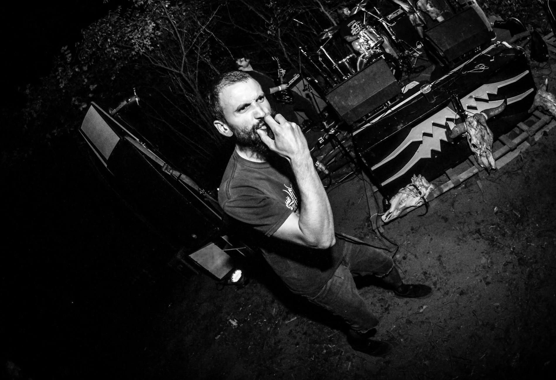 Man with beard scratching his nose at a music event with DJ equipment and animal skulls on the stage.