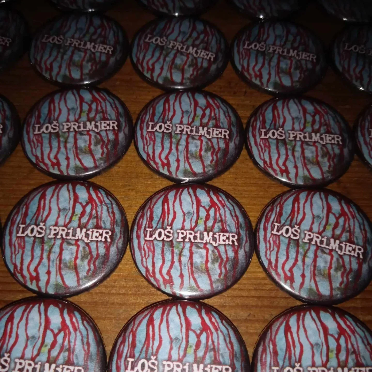 A collection of chocolate coins with a design resembling blood splatters, featuring the text "LOS PRIMJER" on each coin, placed on a wooden surface.