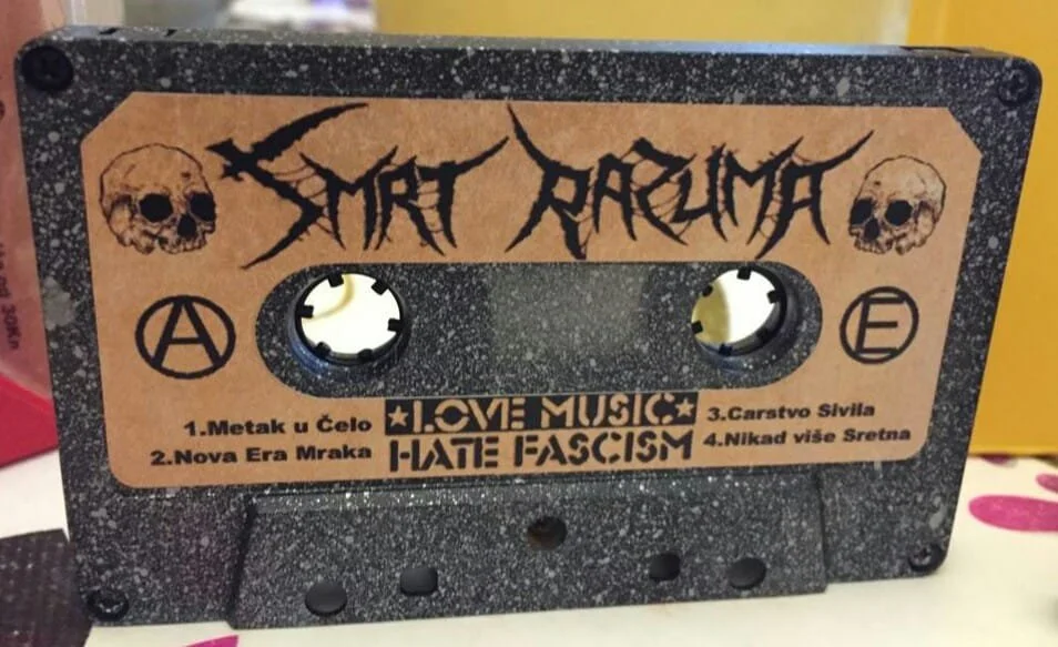 A decorated cassette tape with black and peach colors, featuring skull illustrations and gothic-style text.
