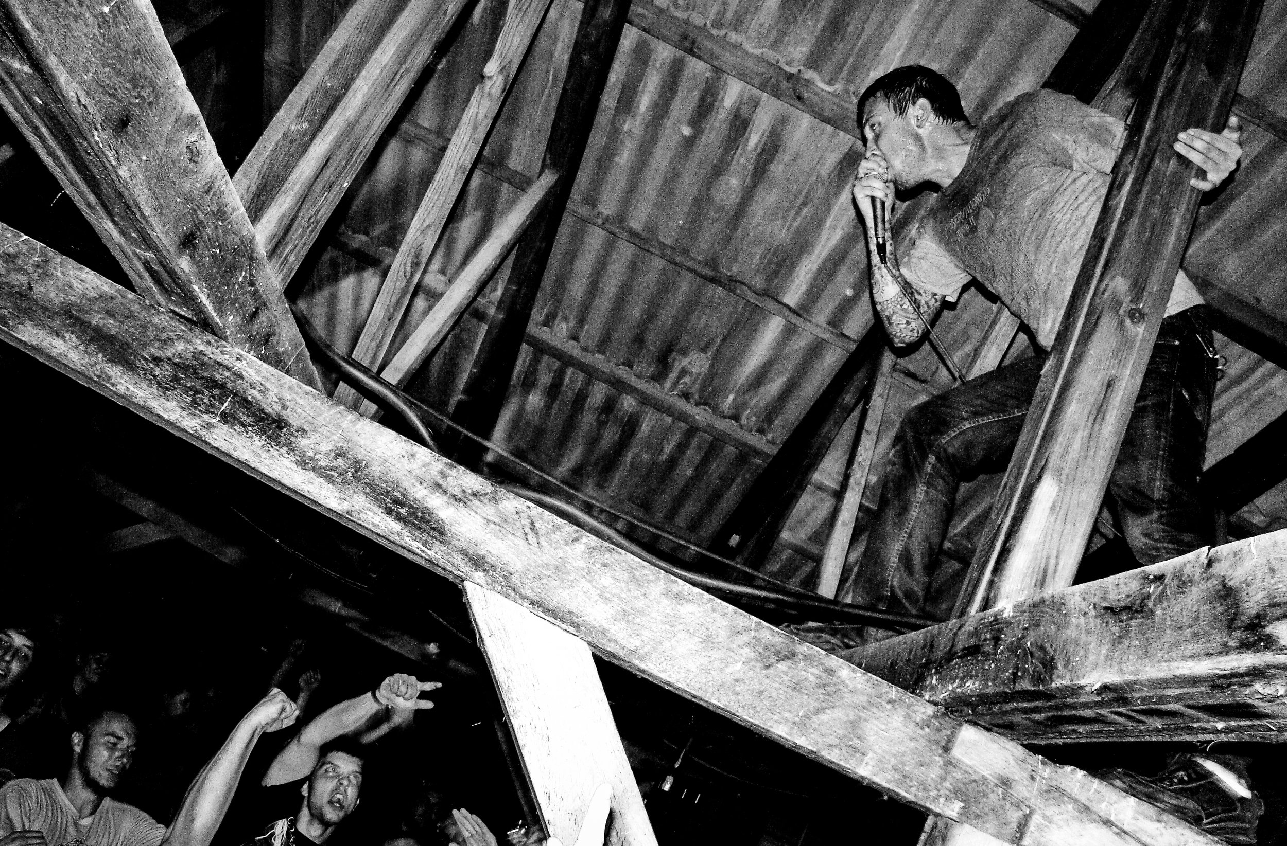 A person with dark hair sings into a microphone on a wooden stage, with an audience reaching towards them in the foreground. Band name: Another Breath