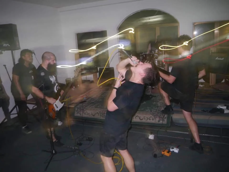A band performs live indoors, with a lead singer passionately singing into a microphone, surrounded by guitarists and drums, with motion blur and light streaks indicating dynamic movement.